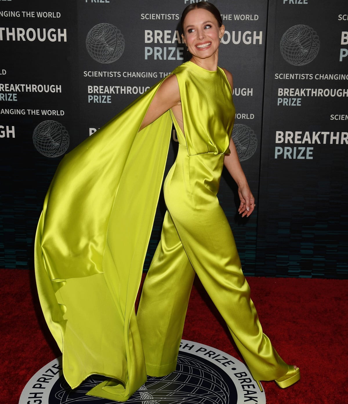 Kristen Bell lights up the red carpet in a vibrant neon Cong Tri jumpsuit with a dramatic cape at the 9th Annual Breakthrough Prize Ceremony