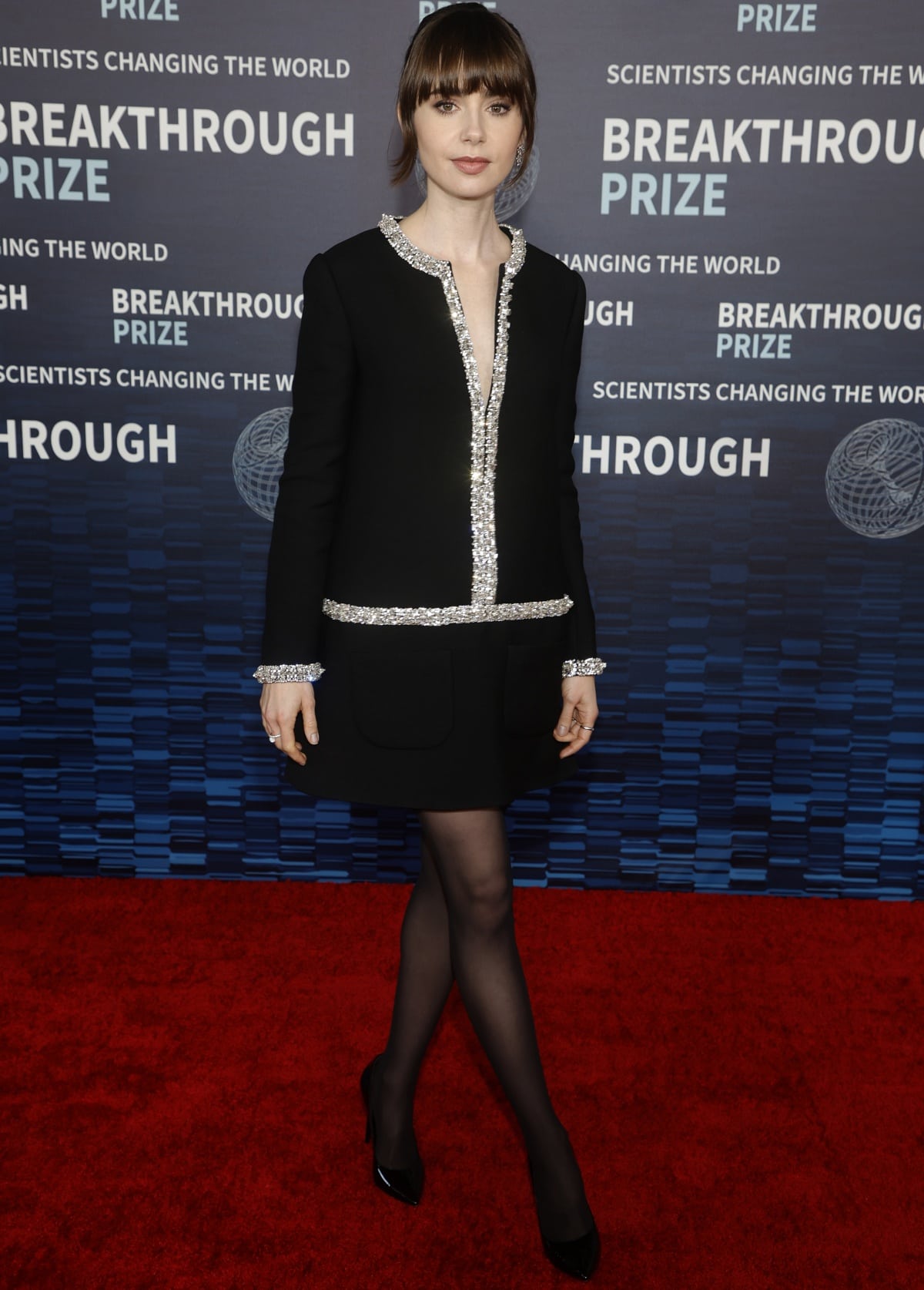 Lily Collins pairs sheer black tights with sleek pointed-toe black pumps, completing her embellished Celine mini dress with understated, leg-lengthening elegance on the red carpet