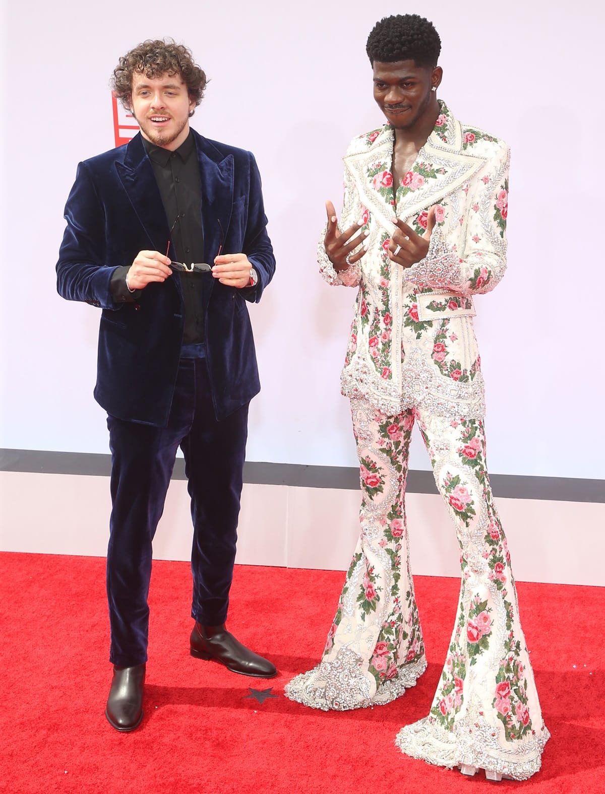 Jack Harlow wearing a navy blue velvet Musika suit with black leather boots, alongside Lil Nas X in a white and pink floral-embroidered ’70s-style suit by Richard Quinn paired with sky-high platform shoes, at the BET Awards 2021