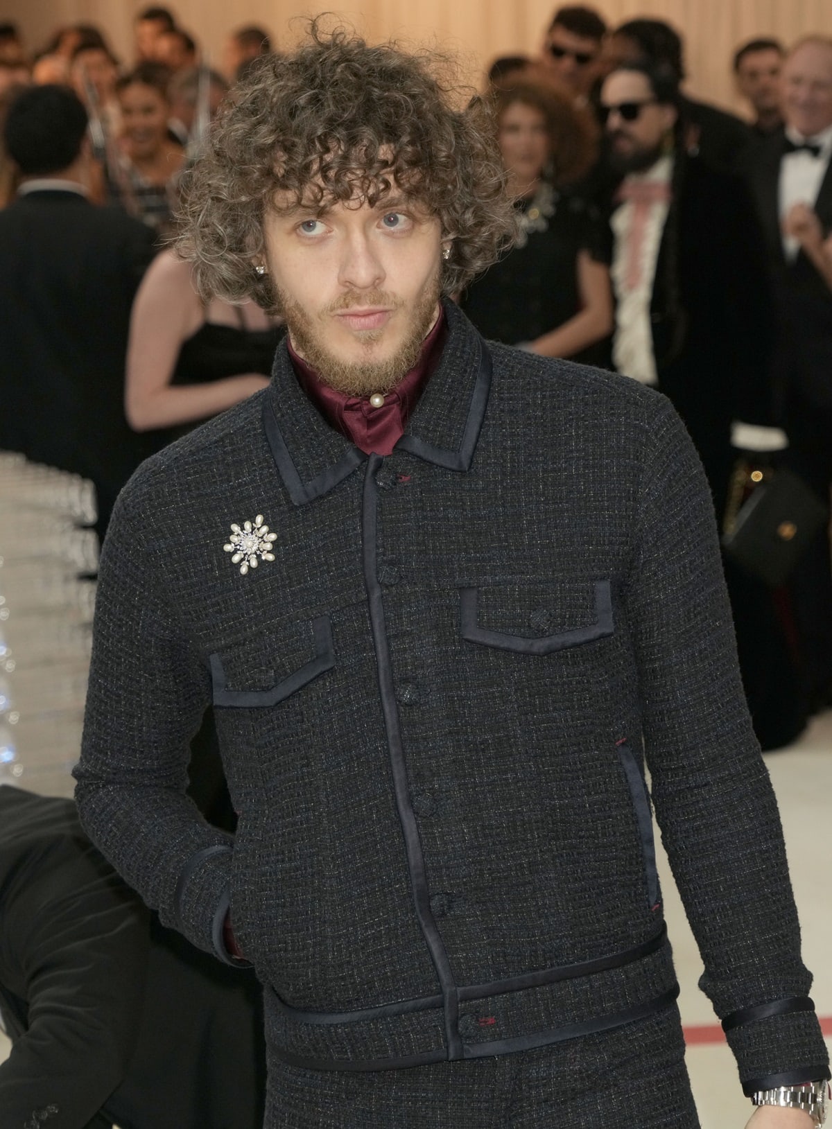 Jack Harlow in a custom navy bouclé Tommy Hilfiger jacket with satin-trimmed details, styled with a burgundy satin shirt, pearl button fastening, and crystal brooch