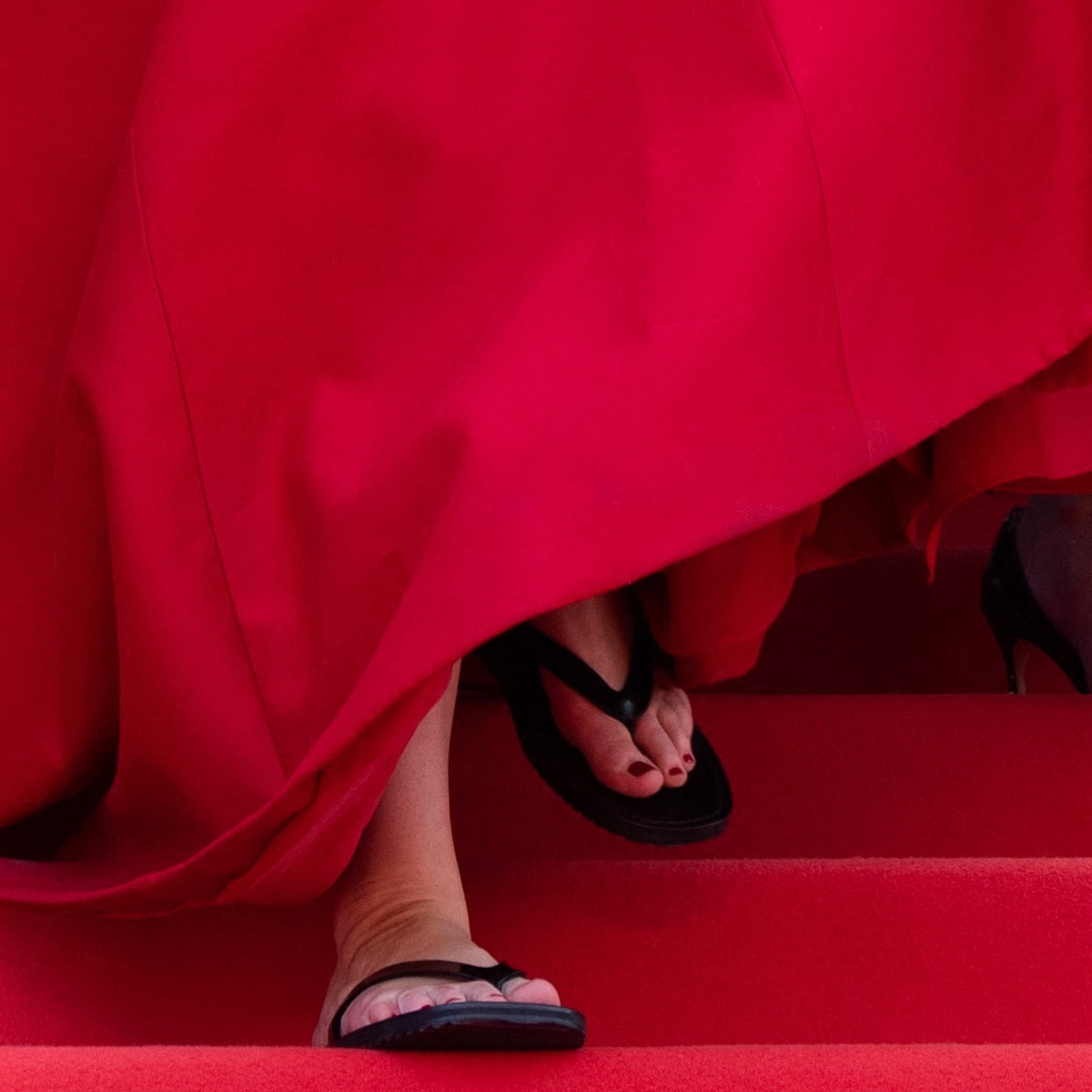 Lifting her hemline, Jennifer Lawrence revealed a pair of black The Row flip-flop sandals underneath her red Christian Dior Couture ball gown
