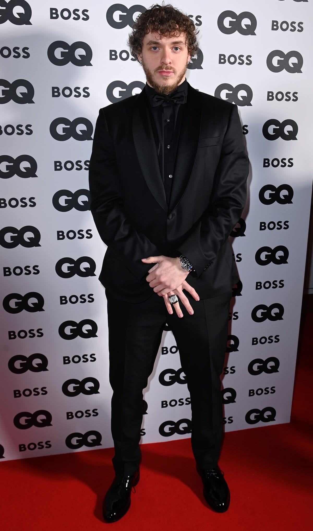 Jack Harlow wearing a sharp black Hugo Boss tuxedo with satin lapels, styled with a bow tie, statement silver ring, luxury watch, and polished black dress shoes at the GQ Men of the Year Awards 2022 held at The Mandarin Oriental Hyde Park in London, England, on November 16, 2022