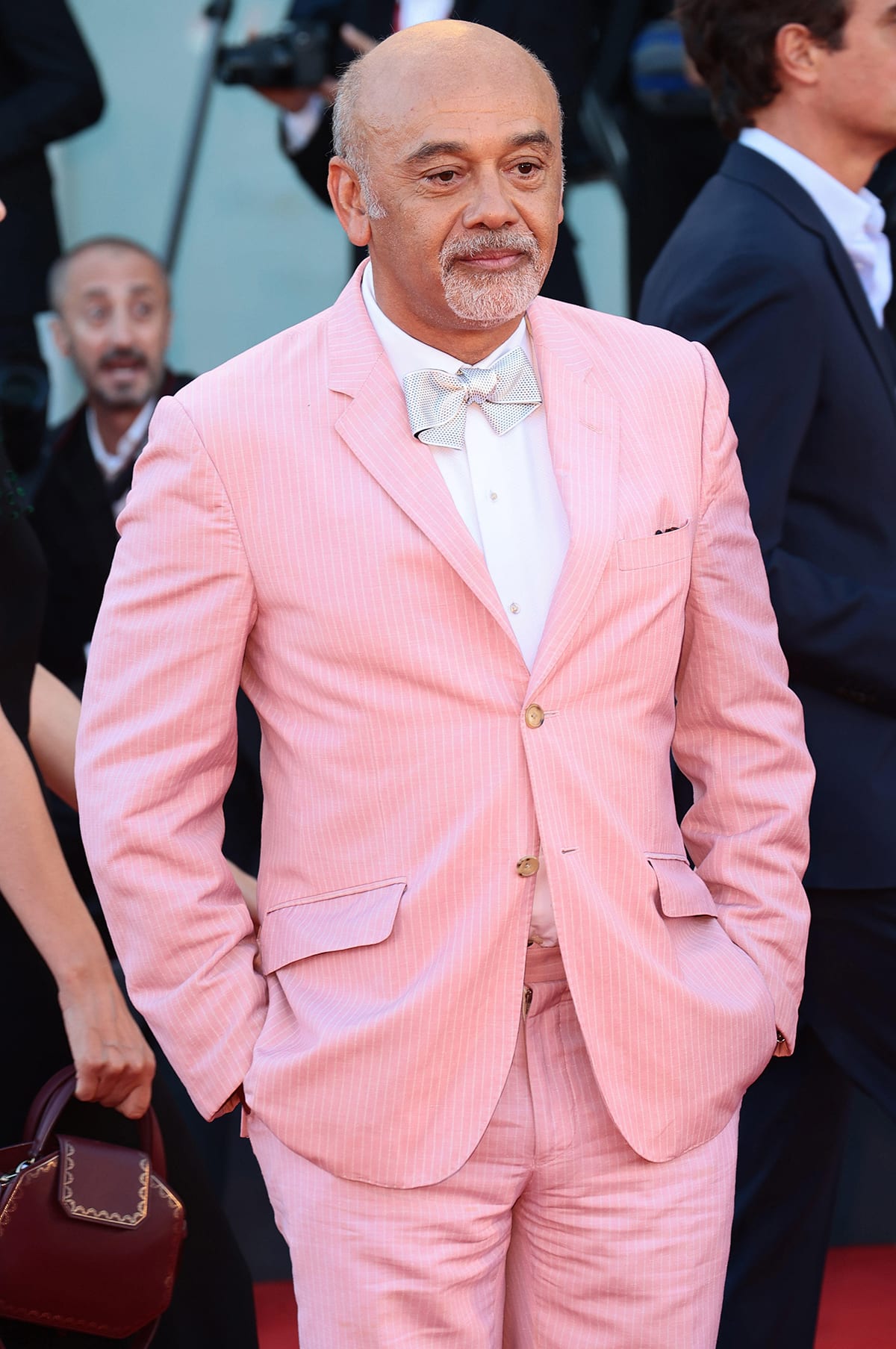 Christian Louboutin, renowned for his iconic red-soled shoes, makes a stylish statement in a pastel pink suit and bow tie at a red carpet event