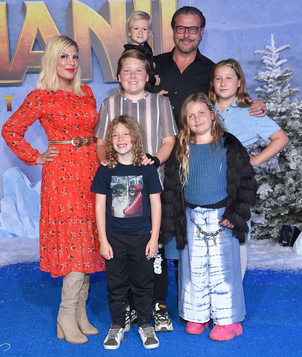 Tori Spelling posed with Dean McDermott and their children at a movie premiere, wearing a red floral midi dress with taupe suede boots, while her kids opted for casual looks in sneakers, tie-dye pants, and playful Crocs