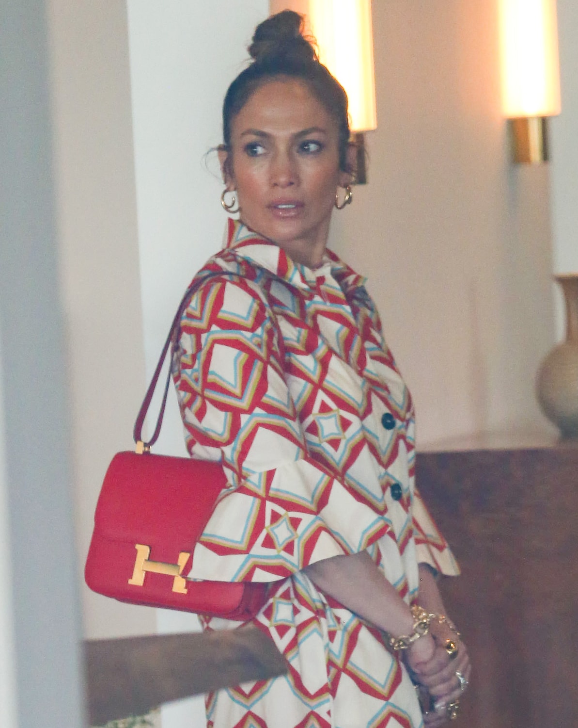 Jennifer Lopez wears a messy topknot and ties her look together with gold jewelry and a red Hermès bag