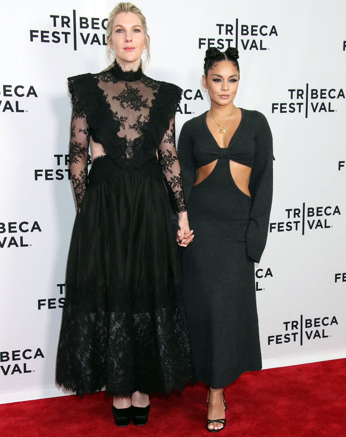 Lily Rabe and Vanessa Hudgens hold hands on the Tribeca Festival red carpet, with Rabe in a black lace Zimmermann gown and platform Jimmy Choo heels, and Hudgens in a charcoal Michael Kors cutout dress paired with Chrissy leather sandals