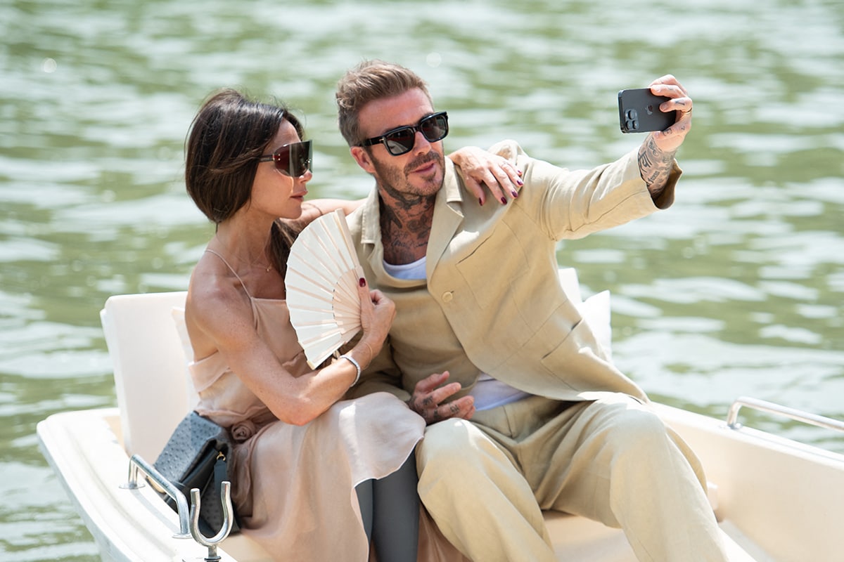 Victoria Beckham carries a fan and structured ostrich bag while posing for a selfie with David Beckham aboard a boat at the Jacquemus “Le Chouchou” Spring 2024 show