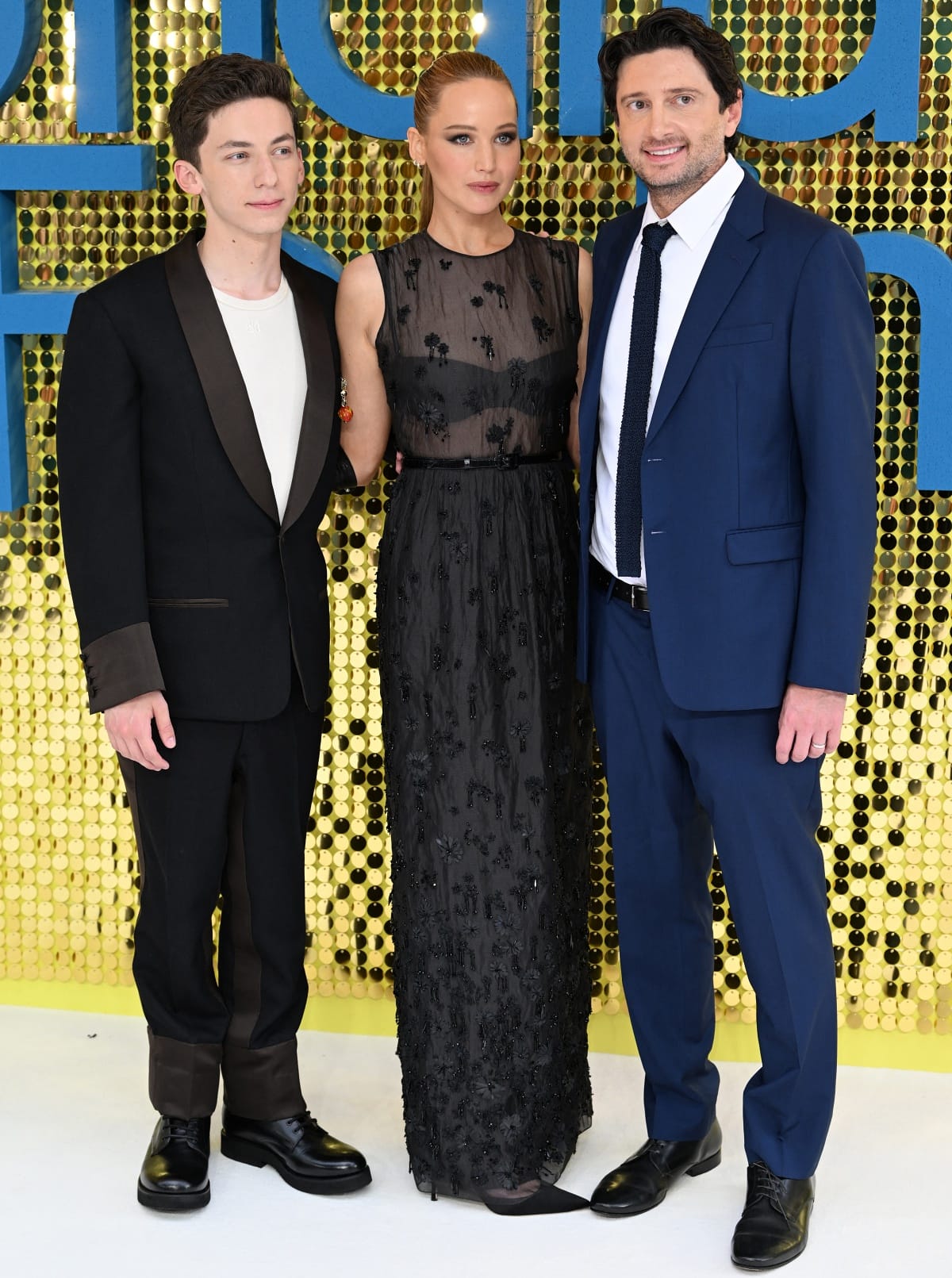 Andrew Barth Feldman, Jennifer Lawrence, and director Gene Stupnitsky pose at the UK premiere of No Hard Feelings, with Lawrence grounding her sheer Dior gown in sleek black pointed-toe slingback pumps