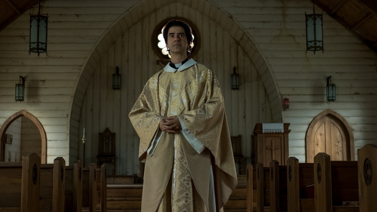 Hamish Linklater as Father Paul Hill in Netflix’s Midnight Mass, wearing ornate gold liturgical vestments while delivering sermons inside the church on Crockett Island