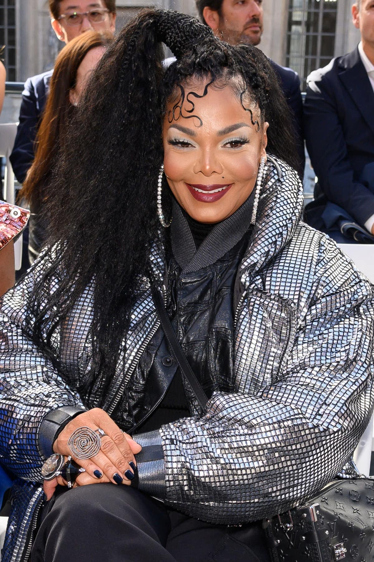 Janet Jackson dazzles in a futuristic metallic puffer jacket, bold spiral rings, and sleek braided ponytail while attending the fashion show