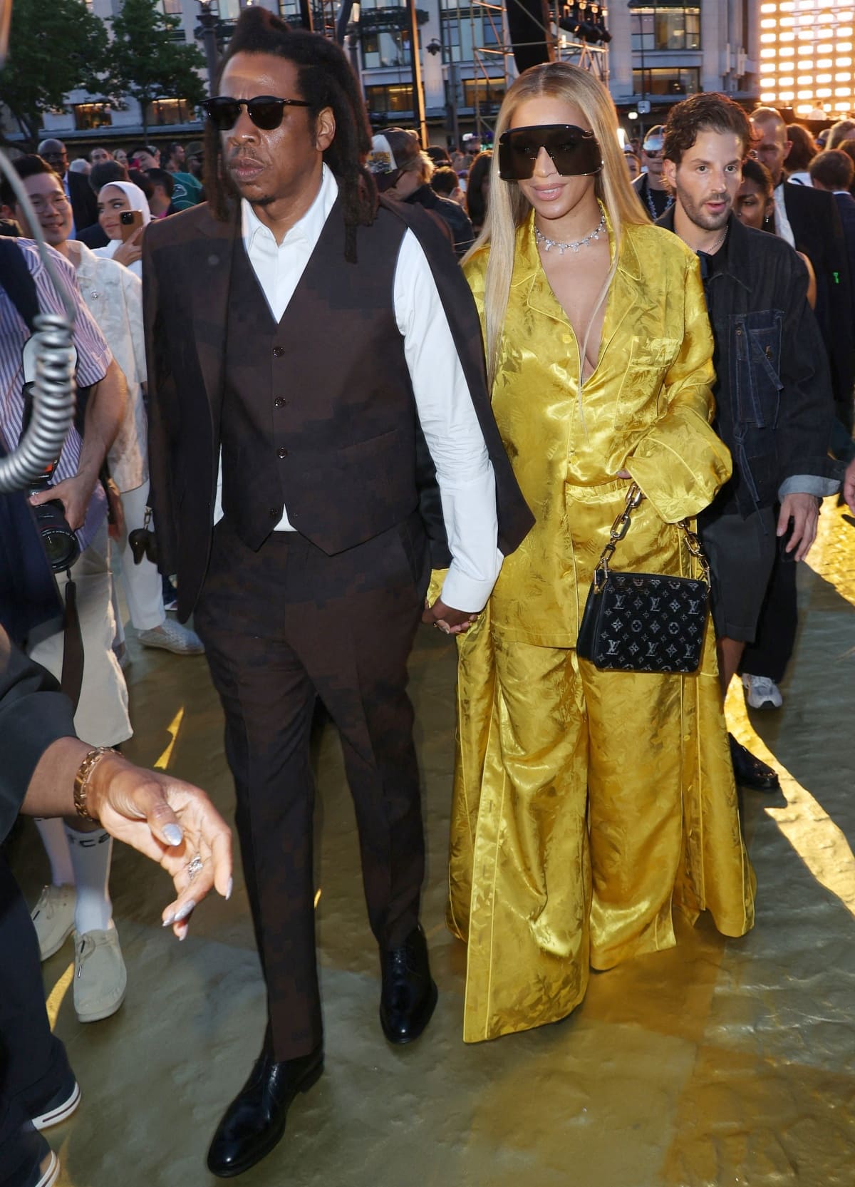 Jay-Z and Beyoncé arrive hand-in-hand at Pharrell Williams’ debut Louis Vuitton menswear show during Paris Fashion Week, with Beyoncé concealing towering platform sandals beneath her flowing gold silk ensemble while Jay-Z paired his relaxed Damier-inspired tailoring with polished black leather dress shoes
