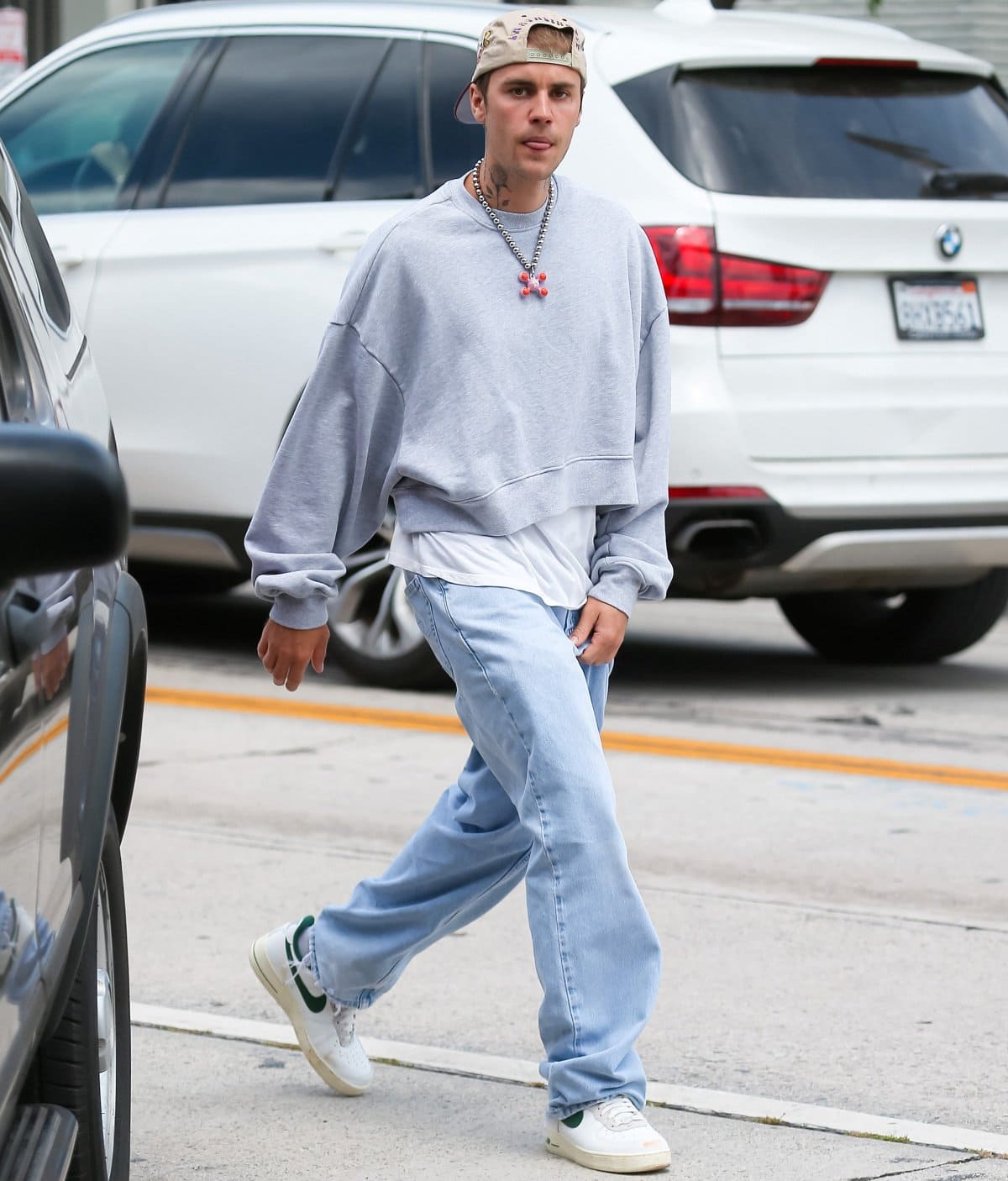 Justin Bieber embraced his laid-back streetwear aesthetic in a gray oversized sweatshirt, loose light-wash jeans, white sneakers with green accents, and a backward baseball cap during his Los Angeles outing
