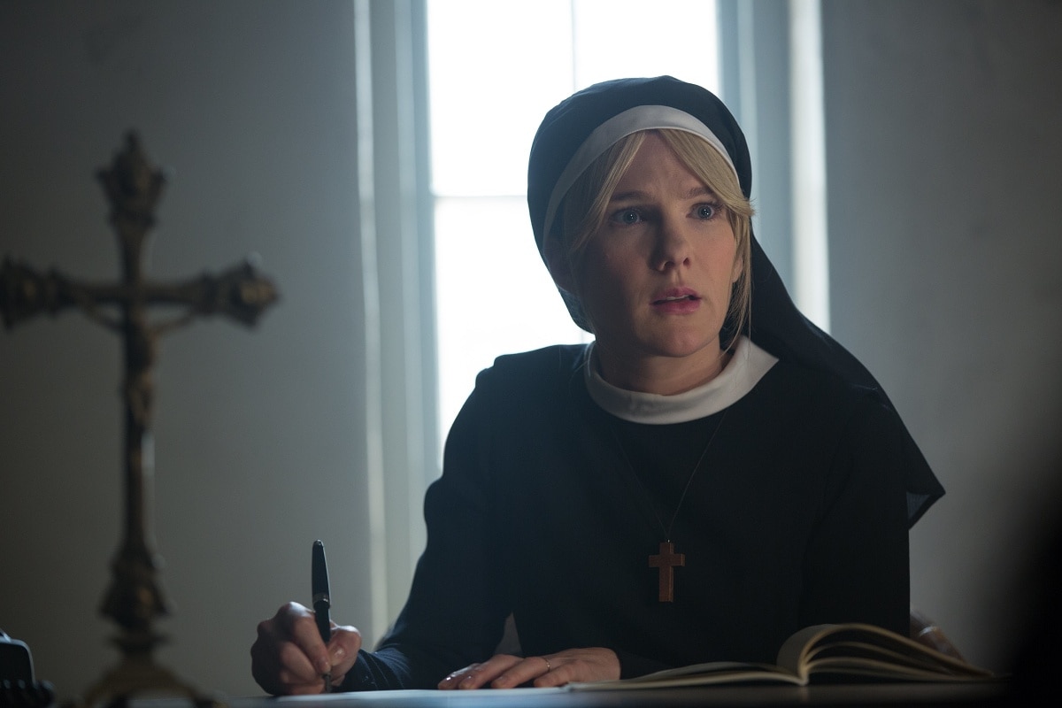 Lily Rabe portraying Sister Mary Eunice in American Horror Story: Asylum, wearing the character’s traditional nun habit with a simple black dress, white wimple, and wooden cross necklace