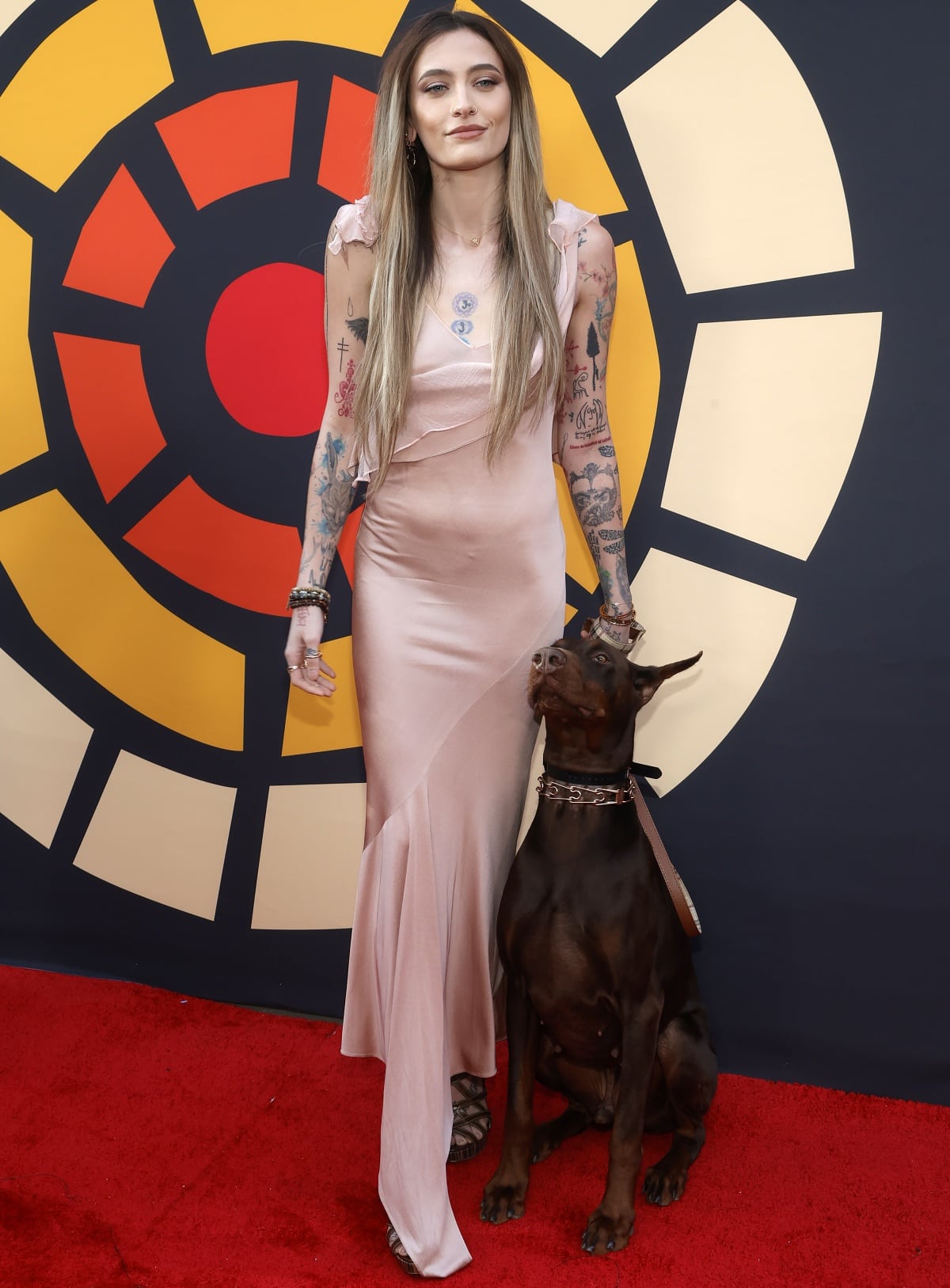 Paris Jackson attends the Charlize Theron Africa Outreach Project 2023 Block Party at Universal Studios Backlot on May 20, 2023, in Universal City, California, wearing a blush pink satin gown and strappy heels, accompanied by her Doberman