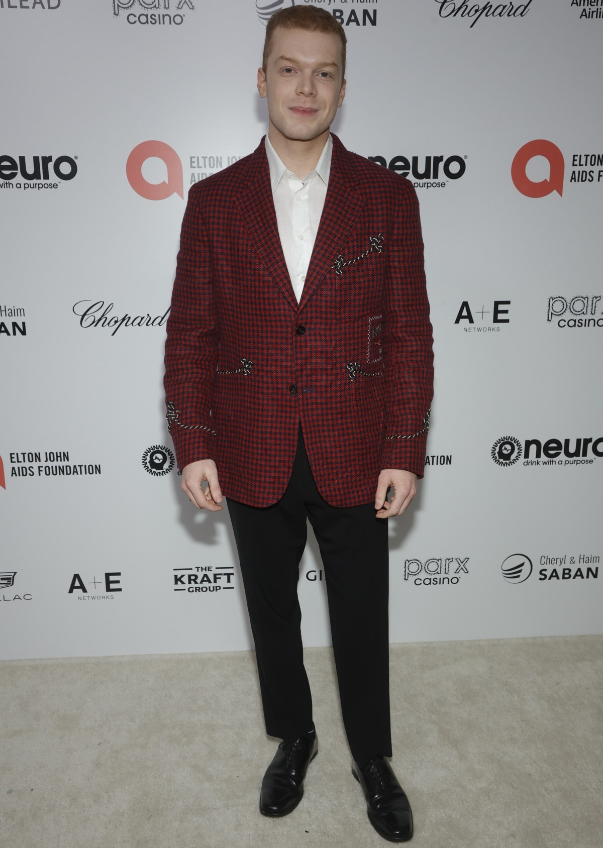 Cameron Monaghan adds a bold twist to classic formalwear in a red-and-black embroidered blazer, crisp white shirt, black trousers, and polished black dress shoes at the 31st Annual Elton John AIDS Foundation Academy Awards Viewing Party in Los Angeles on March 13, 2023
