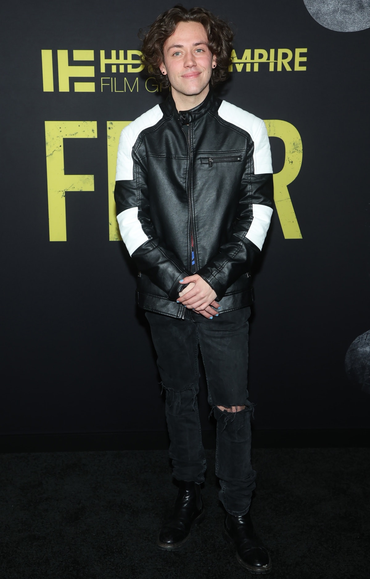 Ethan Cutkosky leans into edgy street style in a black-and-white moto jacket, distressed jeans, and black leather boots at the world premiere of Fear in Los Angeles on January 21, 2023