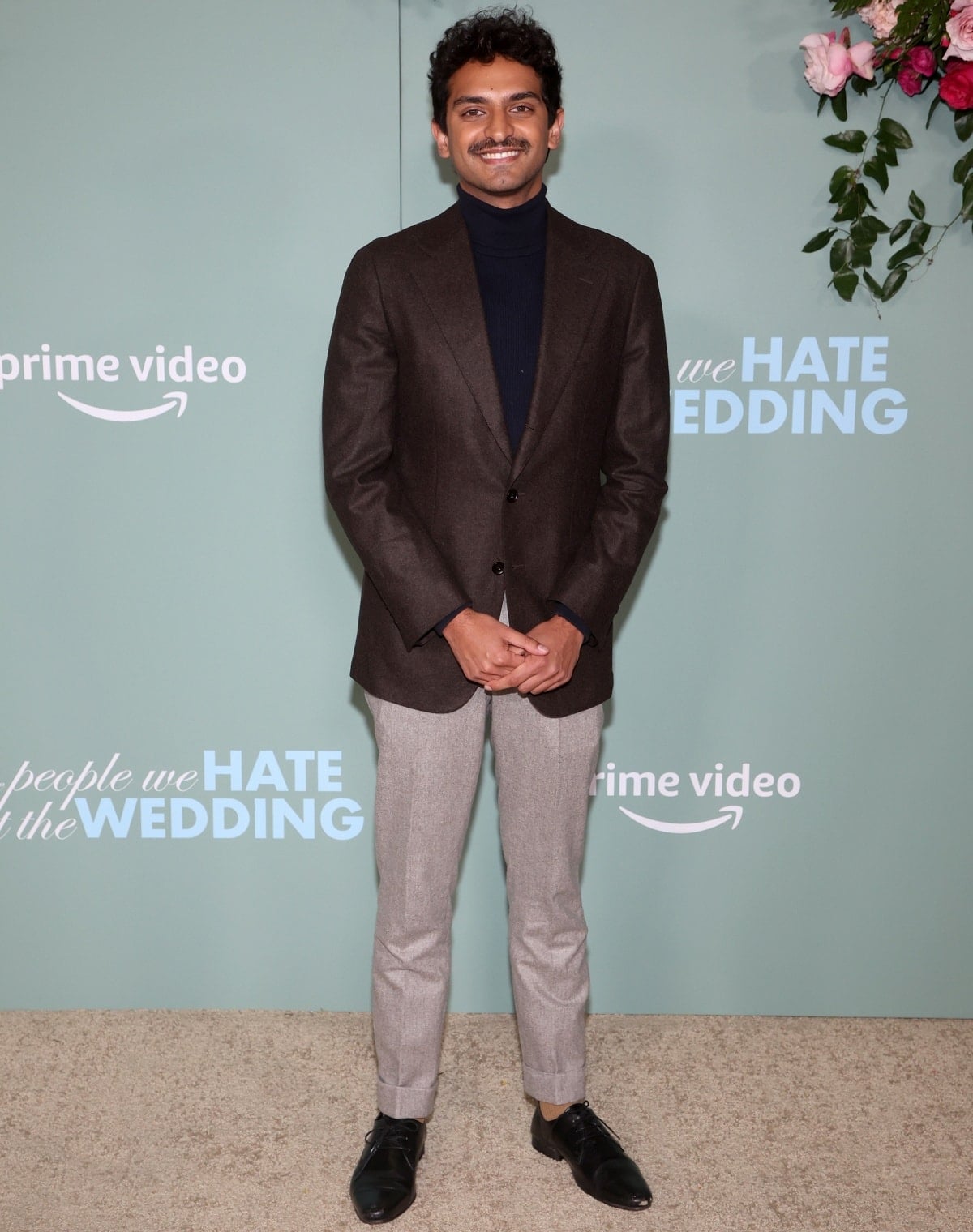 Karan Soni looked effortlessly refined at the Los Angeles premiere of The People We Hate at the Wedding, pairing a chocolate-brown blazer with a navy turtleneck, light gray trousers, and sleek black leather dress shoes.