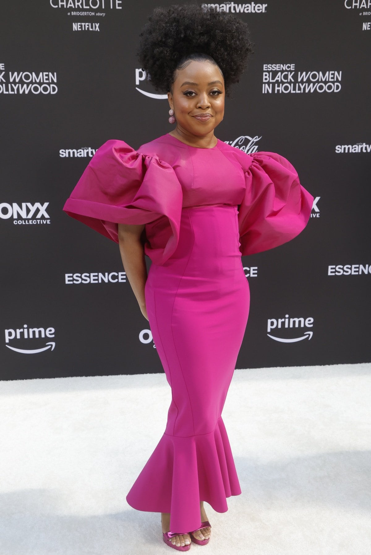 Quinta Brunson dazzled in a vibrant fuchsia gown with dramatic puff sleeves and a flared hem, pairing the bold look with metallic pink open-toe heels at the Essence Black Women in Hollywood event
