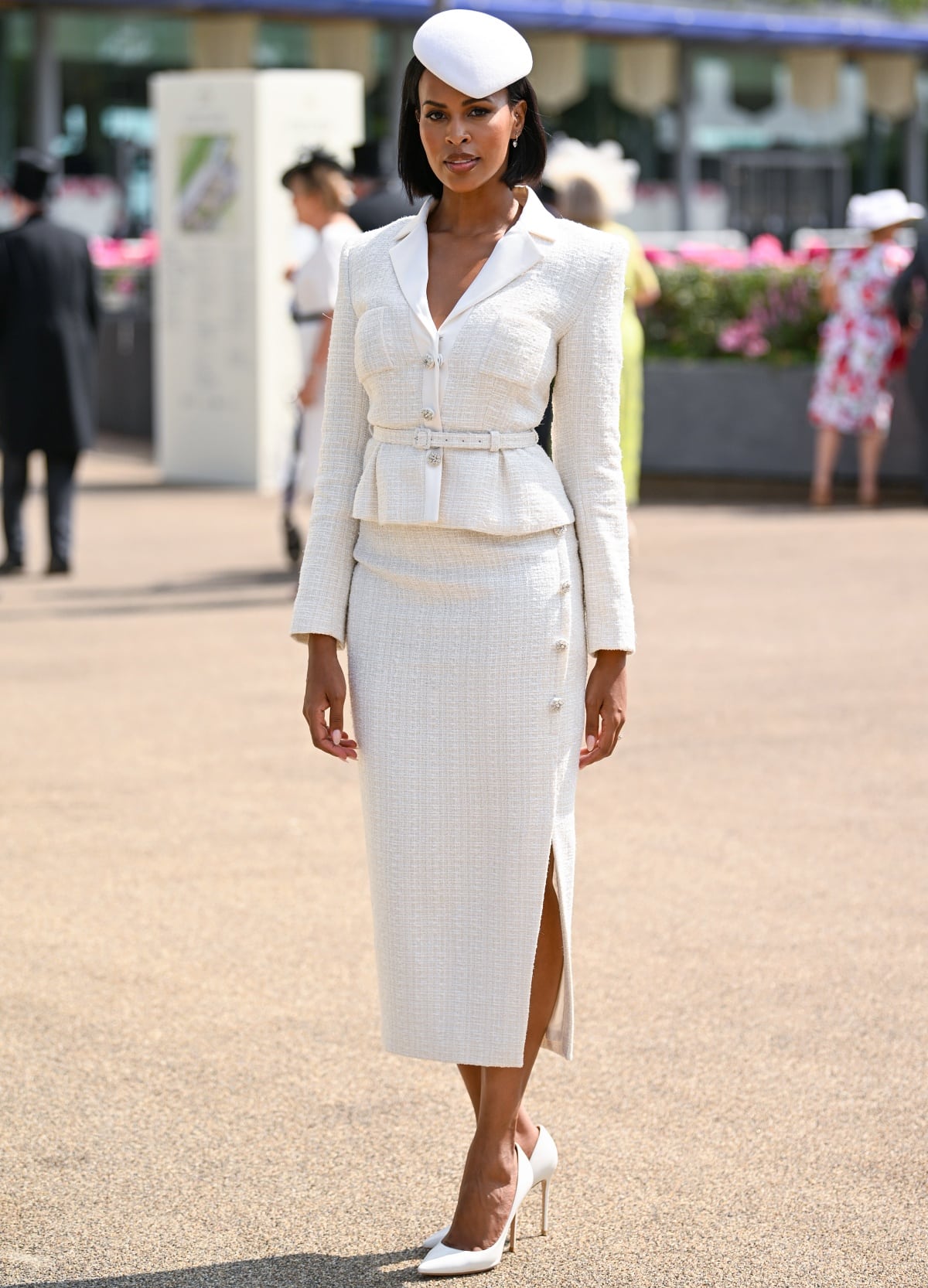 Sabrina Dhowre Elba attended Royal Ascot at Ascot Racecourse on June 22, 2023, for the event’s third day, wearing a custom Self-Portrait bouclé skirt suit by designer Han Chong, featuring a belted peplum jacket and slit pencil skirt with crystal buttons, paired with a white fascinator, diamond dangle earrings, and sleek white pointed-toe pumps