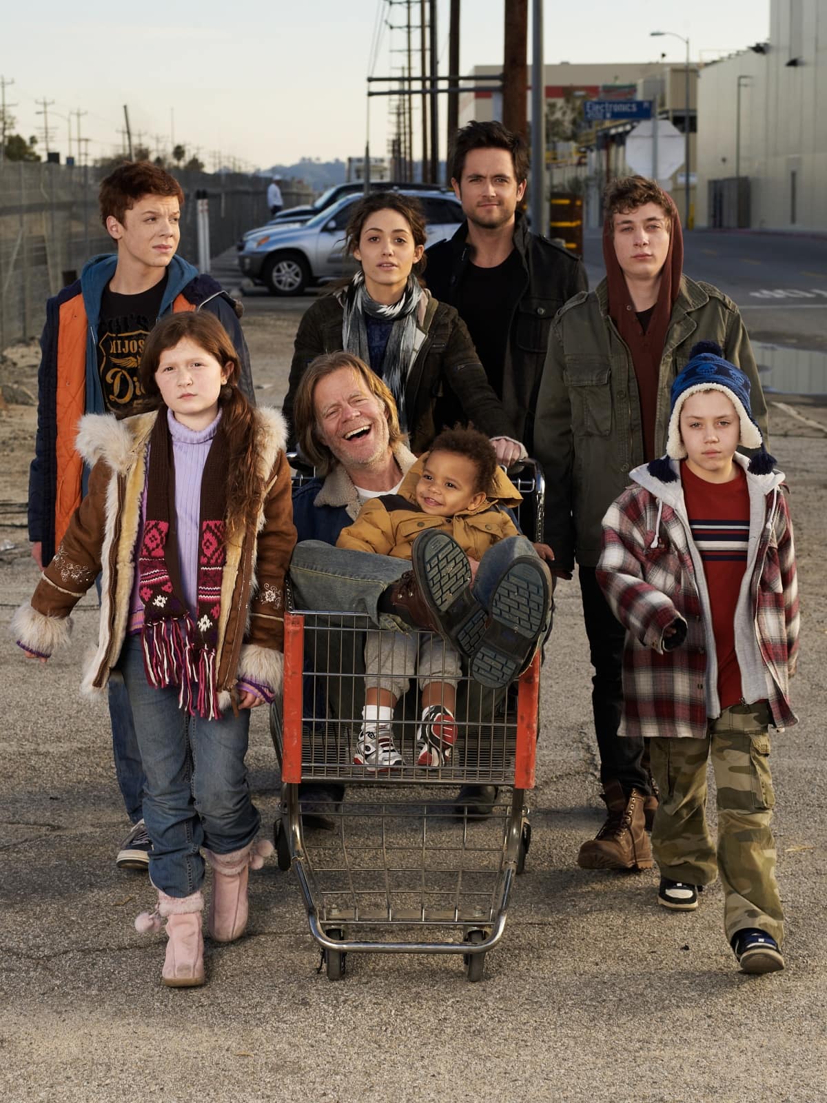 The Gallagher family cast of Shameless pose in rugged, mismatched streetwear—shearling boots, sneakers, and worn layers—capturing the show’s gritty yet authentic Chicago vibe