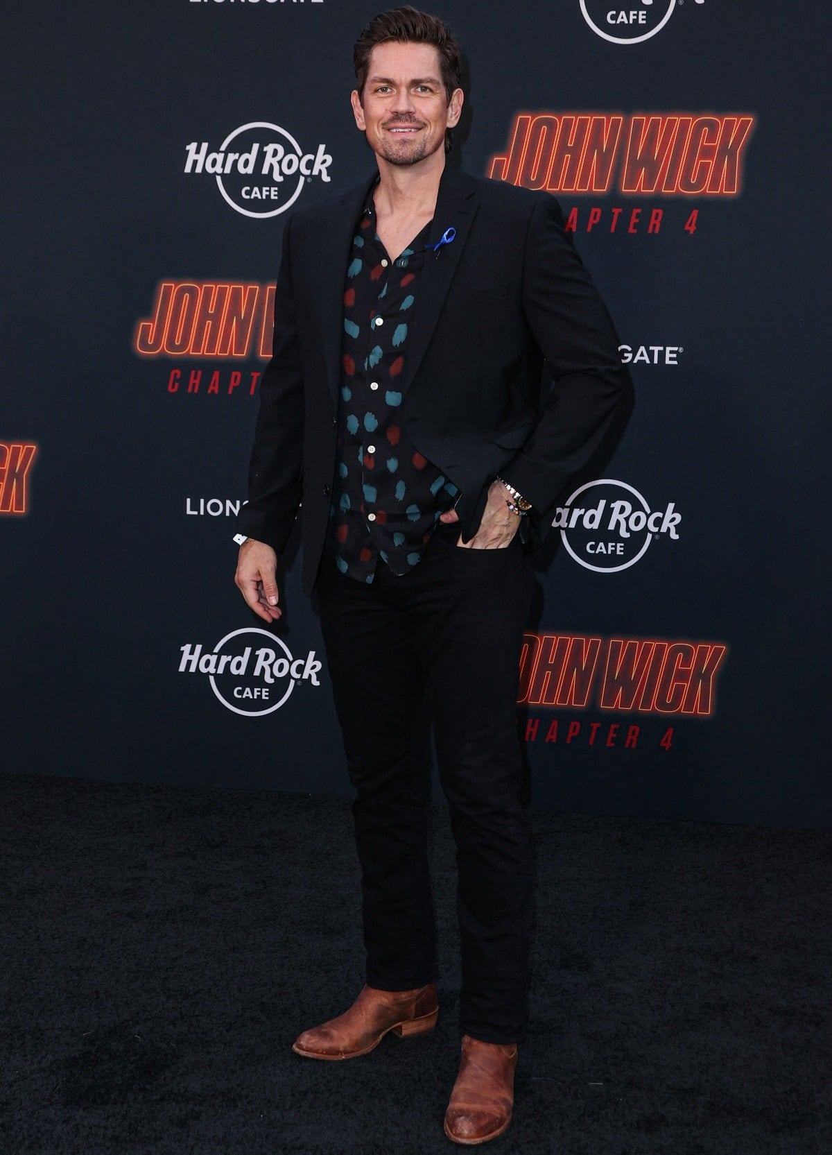 Steve Howey adds a rugged touch to his red carpet look in a patterned shirt, black suit, and worn-in brown leather boots at the John Wick: Chapter 4 premiere in Los Angeles on March 21, 2023