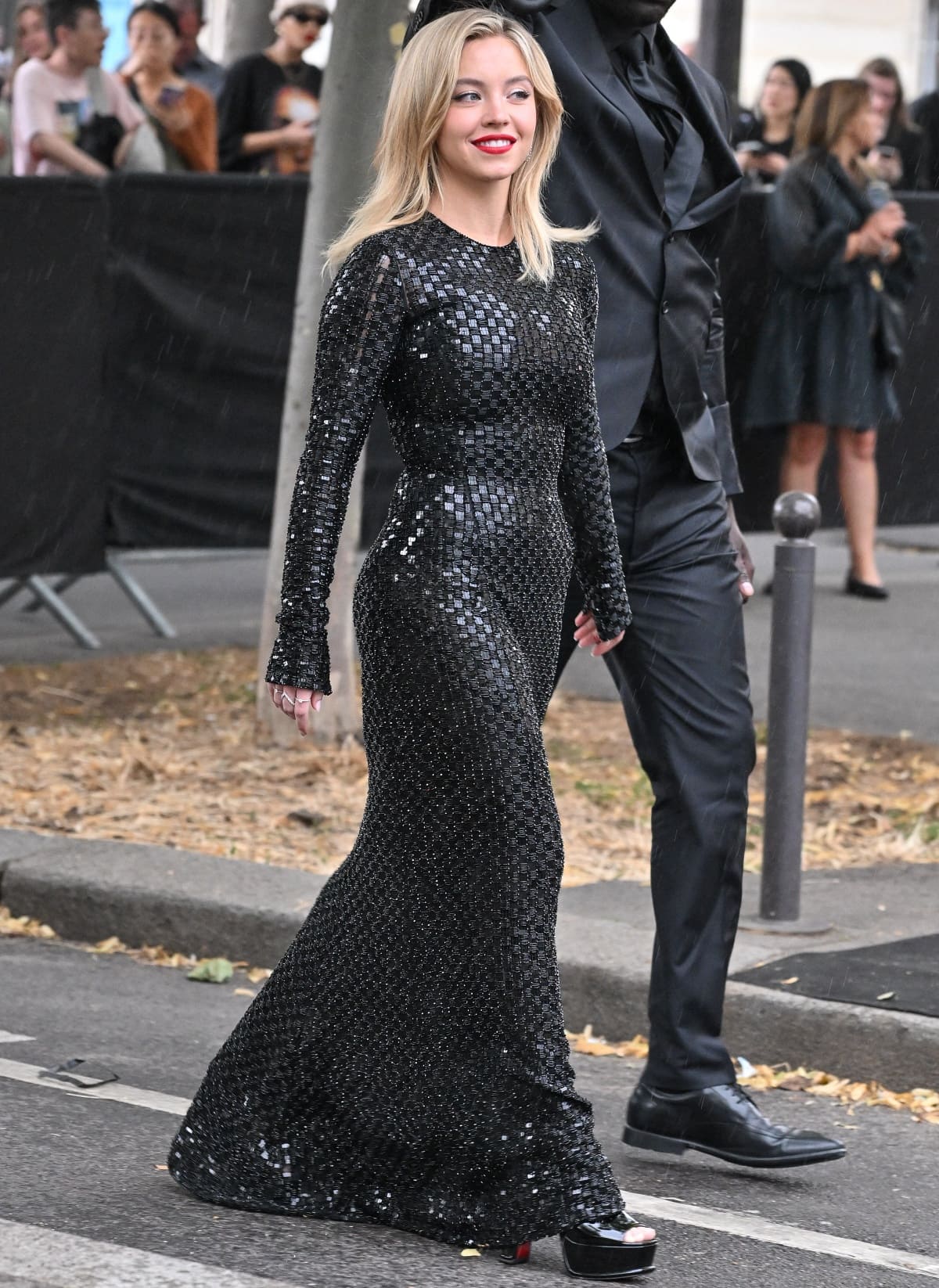 Sydney Sweeney arriving at the Giorgio Armani Privè Fall/Winter 2024 show in Paris, stepping out in glossy black platform heels with a bold red sole that gave her petite frame a dramatic boost and perfectly balanced the elegance of her sequined gown