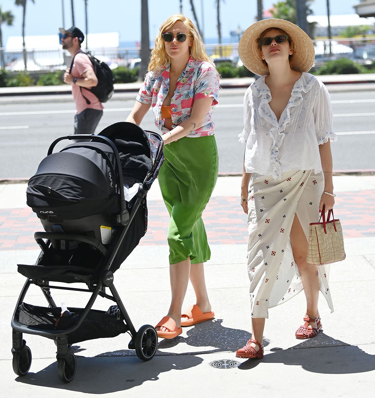 Rumer Willis and her sister Tallulah embrace effortless summer style by the beach, pairing their breezy outfits with vibrant sandals—Rumer in bold orange slides and Tallulah in red woven jelly flats