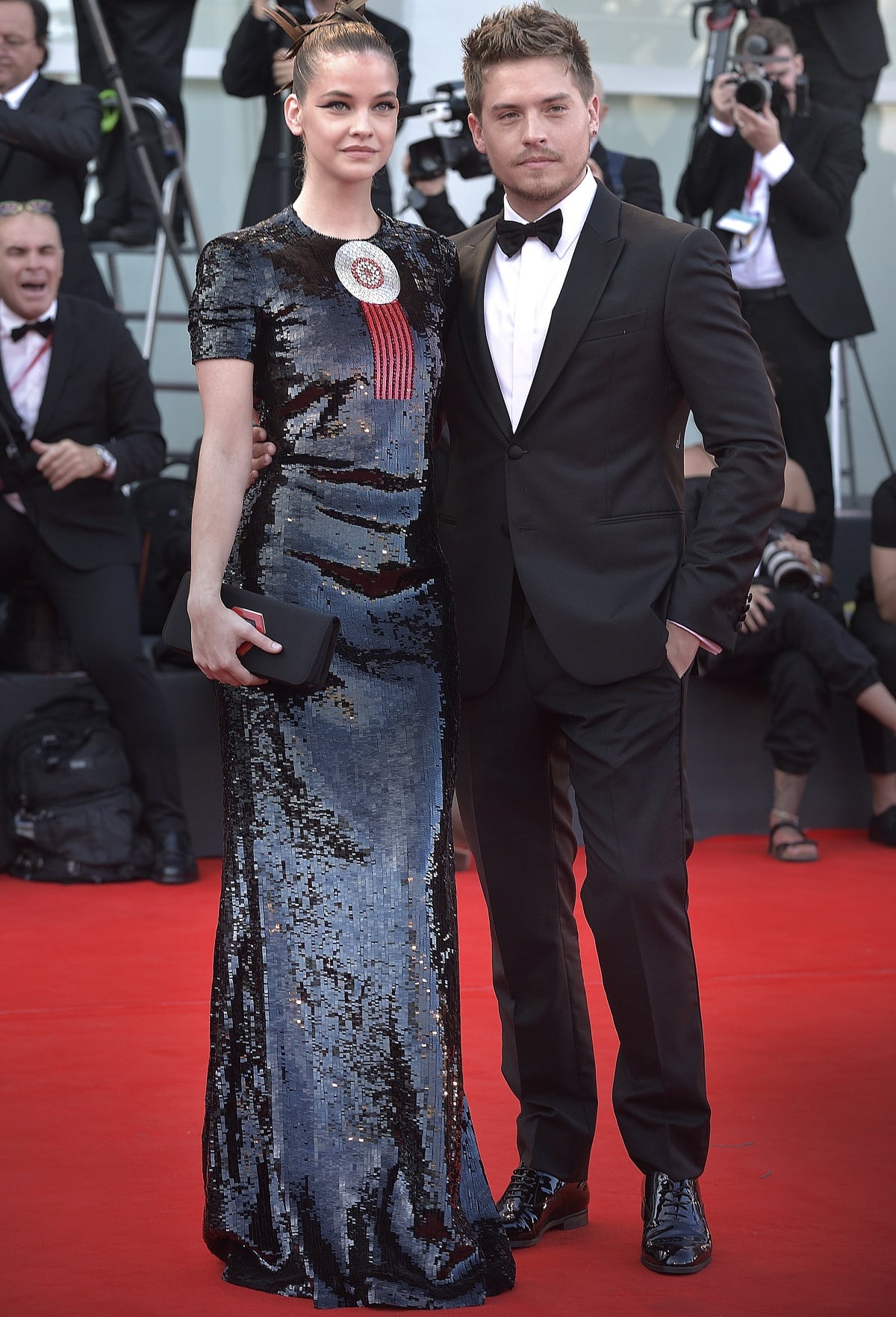 Barbara Palvin dazzles in a sleek sequined Giorgio Armani Privé gown with a statement brooch while Dylan Sprouse opts for a classic black tuxedo and polished dress shoes at the Venice Film Festival