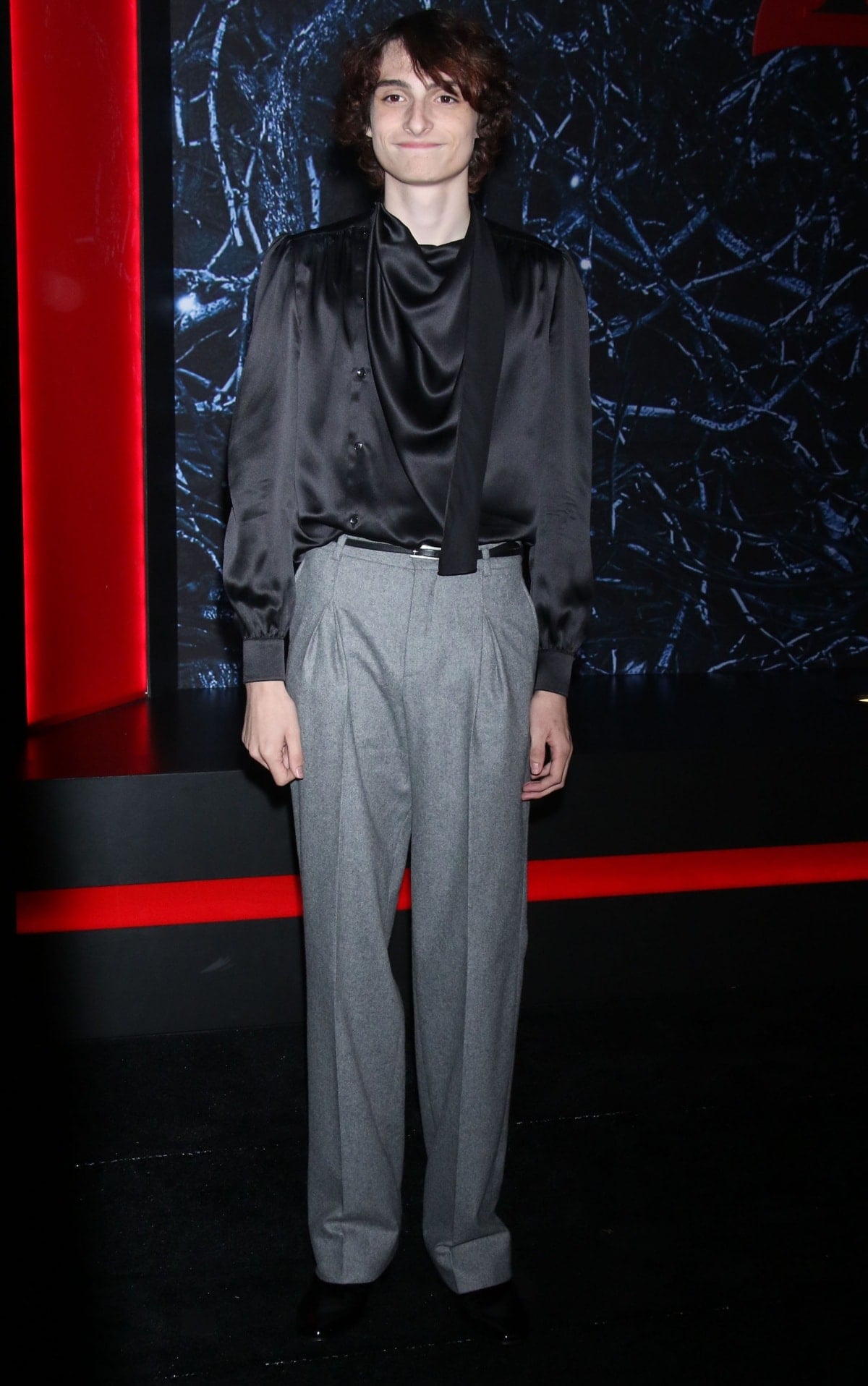 Finn Wolfhard embraced Saint Laurent’s signature aesthetic in a black satin shirt, pleated gray trousers, and glossy black shoes—an understated look that echoed his modeling work with the brand