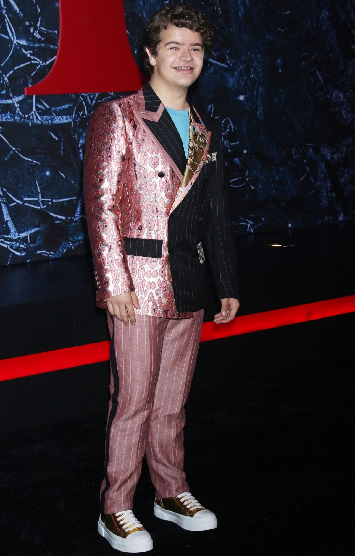 Gaten Matarazzo turned heads in a split-pattern Dolce Gabbana suit made from recycled materials, completing the look with metallic gold platform sneakers for a playful, eco-conscious twist
