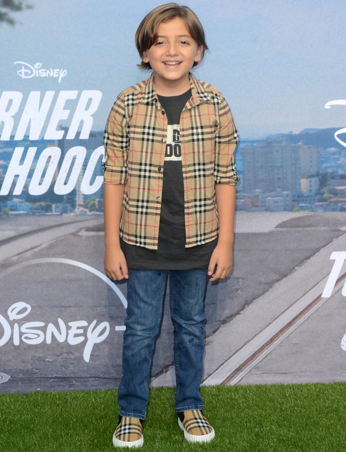 Jeremy Maguire looks adorable in a Burberry check shirt and matching slip-on sneakers, styled with a black graphic tee and classic blue jeans for a polished yet playful red carpet outfit