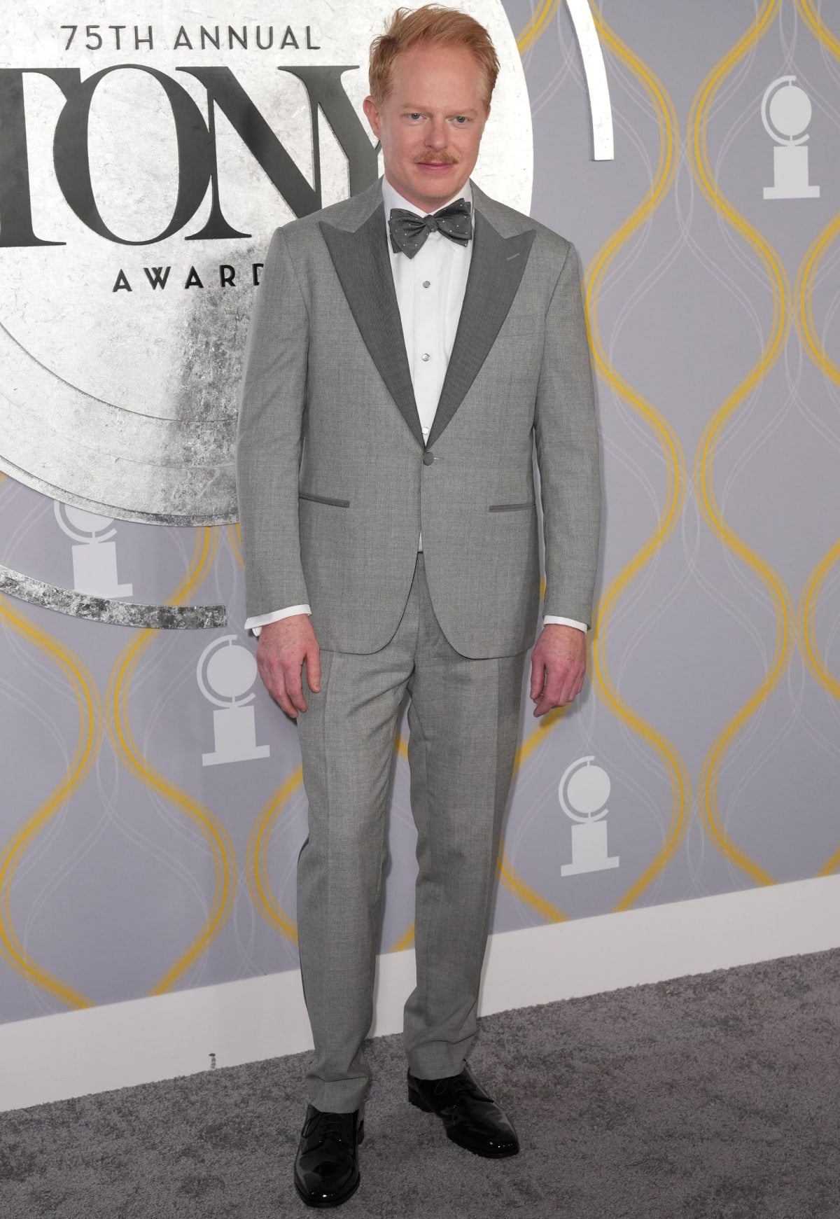 Jesse Tyler Ferguson brings classic elegance to the red carpet in a sharp light gray tuxedo with contrast lapels, finished with glossy black dress shoes that add a polished touch to the formal ensemble