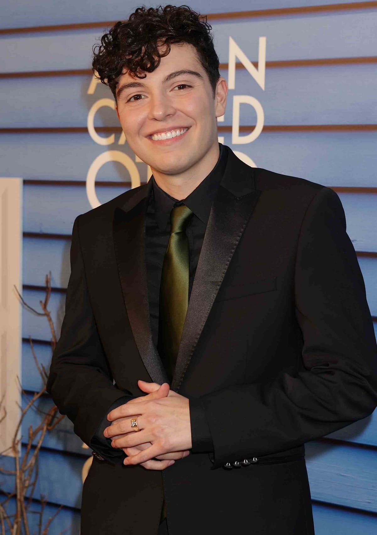 Mack Bayda looked sharp and confident in a sleek black tuxedo with satin lapels and an olive green tie