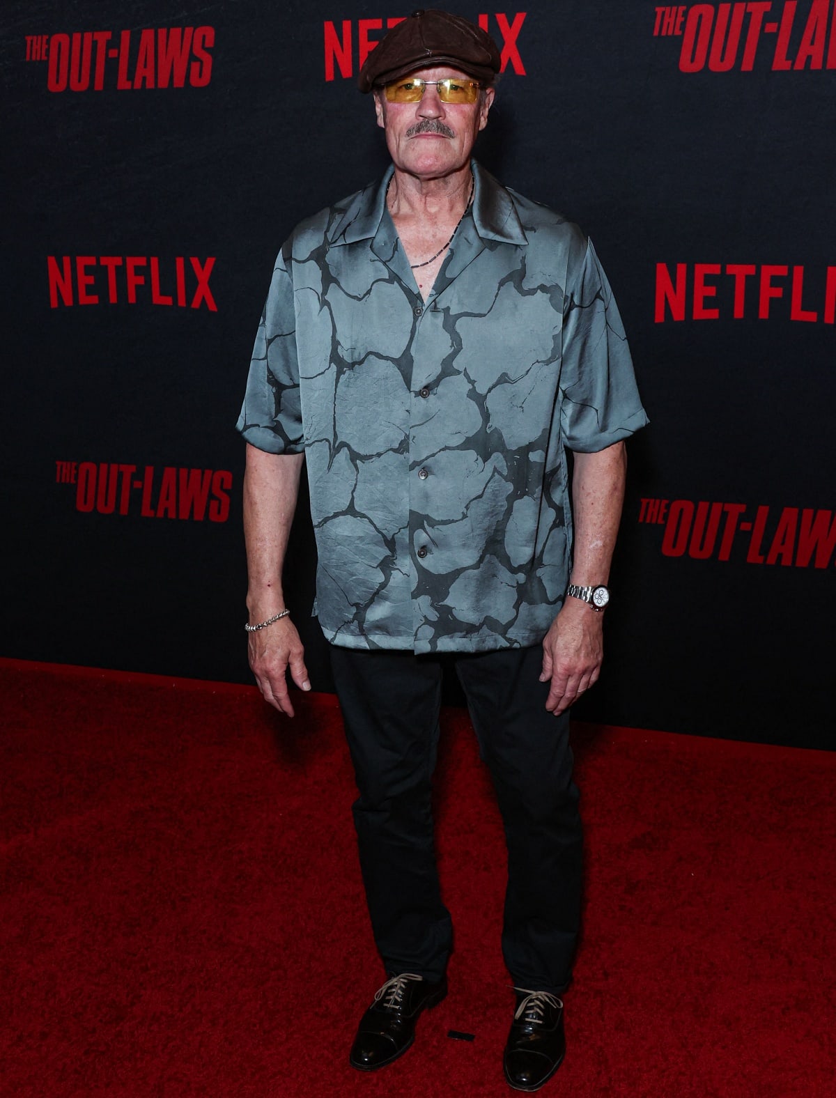 Michael Rooker brings his signature style to The Out-Laws premiere, wearing a relaxed patterned shirt, black pants, and accessorizing with a flat cap and tinted glasses for a cool, laid-back vibe