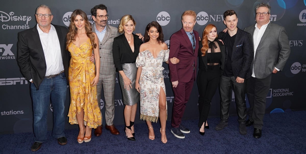 The cast of Modern Family reunites in striking red carpet looks—Sofía Vergara stuns in a yellow floral dress and platform heels, Sarah Hyland dazzles in an off-shoulder floral mini, while the rest of the ensemble showcases sleek suits and sophisticated eveningwear