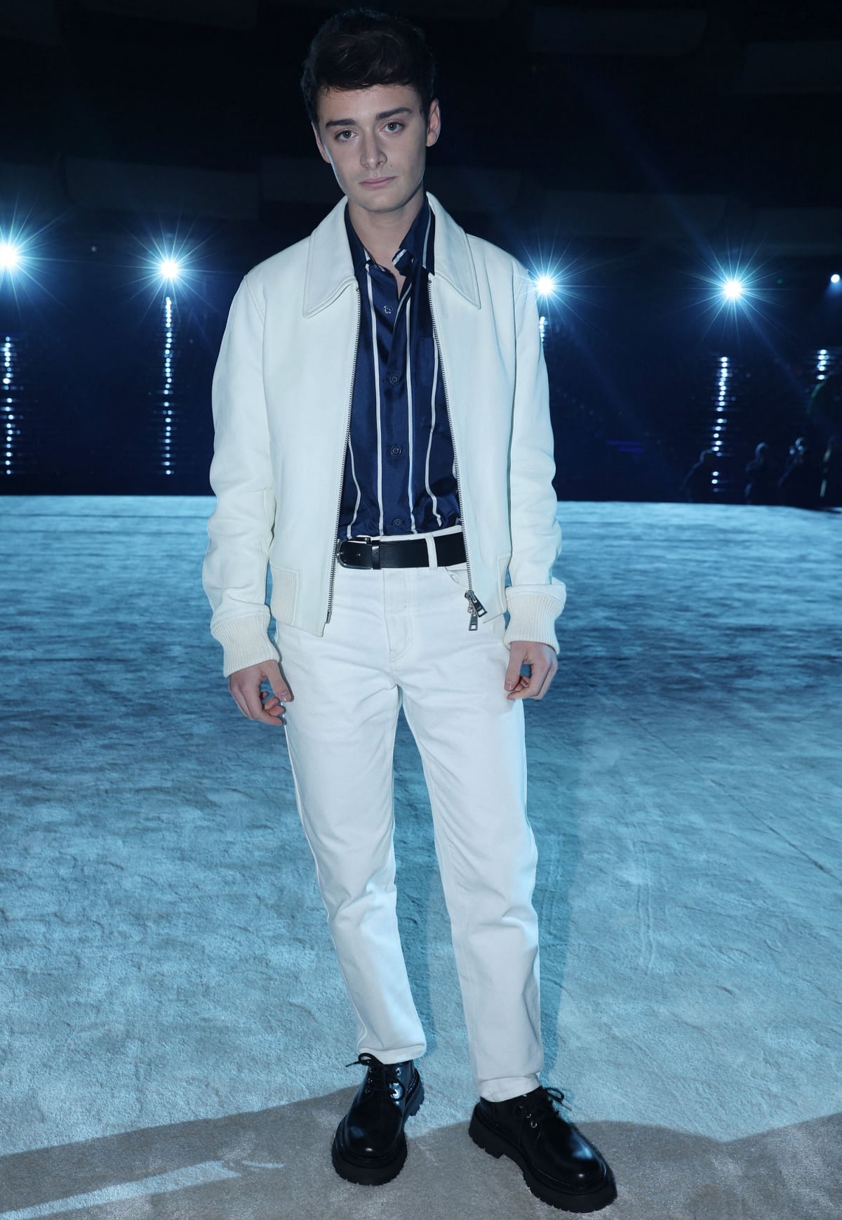 Noah Schnapp attended the AMI – Alexandre Mattiussi Fall/Winter 2023–2024 menswear show at Paris Fashion Week in a sharp white-and-navy look, grounded with chunky black lace-up shoes for a modern edge