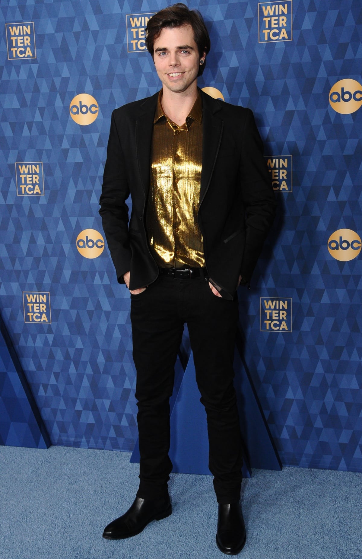 Reid Ewing brings rocker edge to the red carpet in a metallic gold shirt under a sleek black blazer, anchored by slim black pants and polished black leather Chelsea boots