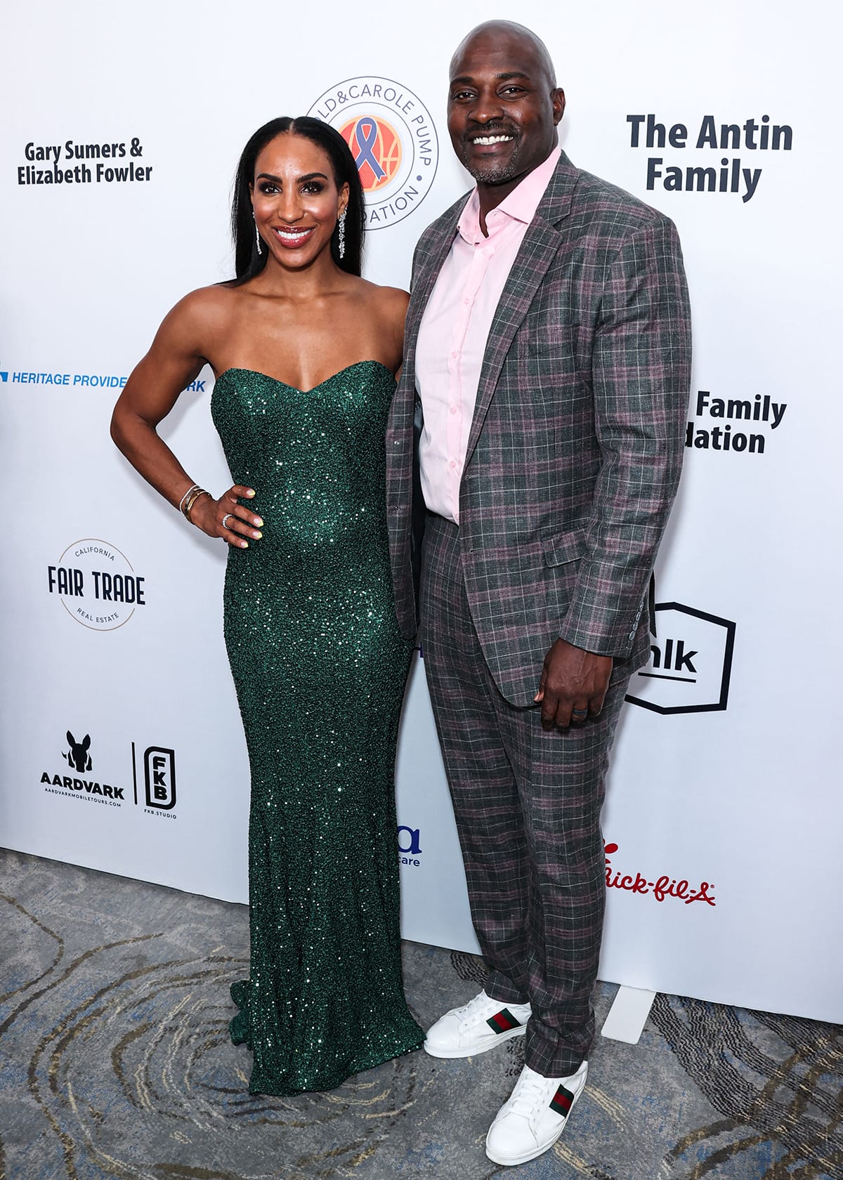 Annemarie Wiley sparkles in a strapless, emerald green sequined gown while posing with husband Marcellus Wiley, who complements her glam look in a plaid suit with crisp white Gucci sneakers