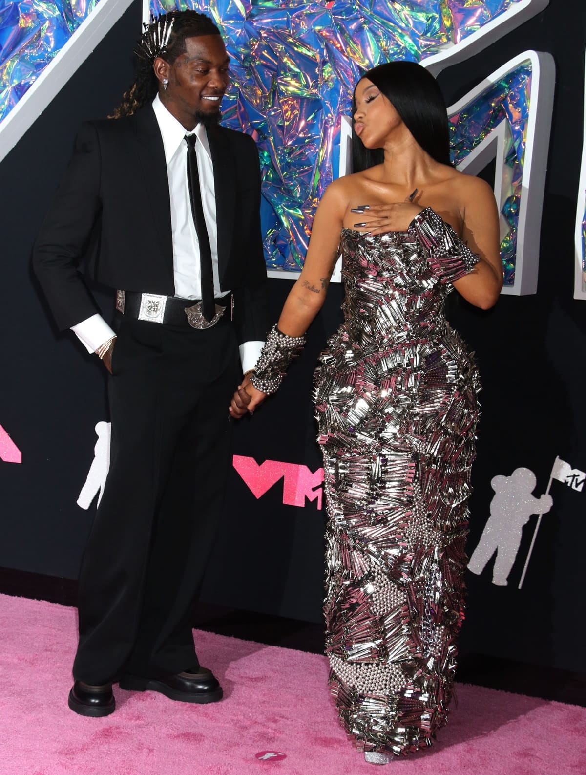 Cardi B and Offset indulged in some flirty fun on the pink carpet at the 2023 MTV Video Music Awards, where her glitter-tipped heels peeked out beneath a sculptural Dilara Findikoglu gown, while Offset grounded his sharp tailored look with sleek black platform loafers