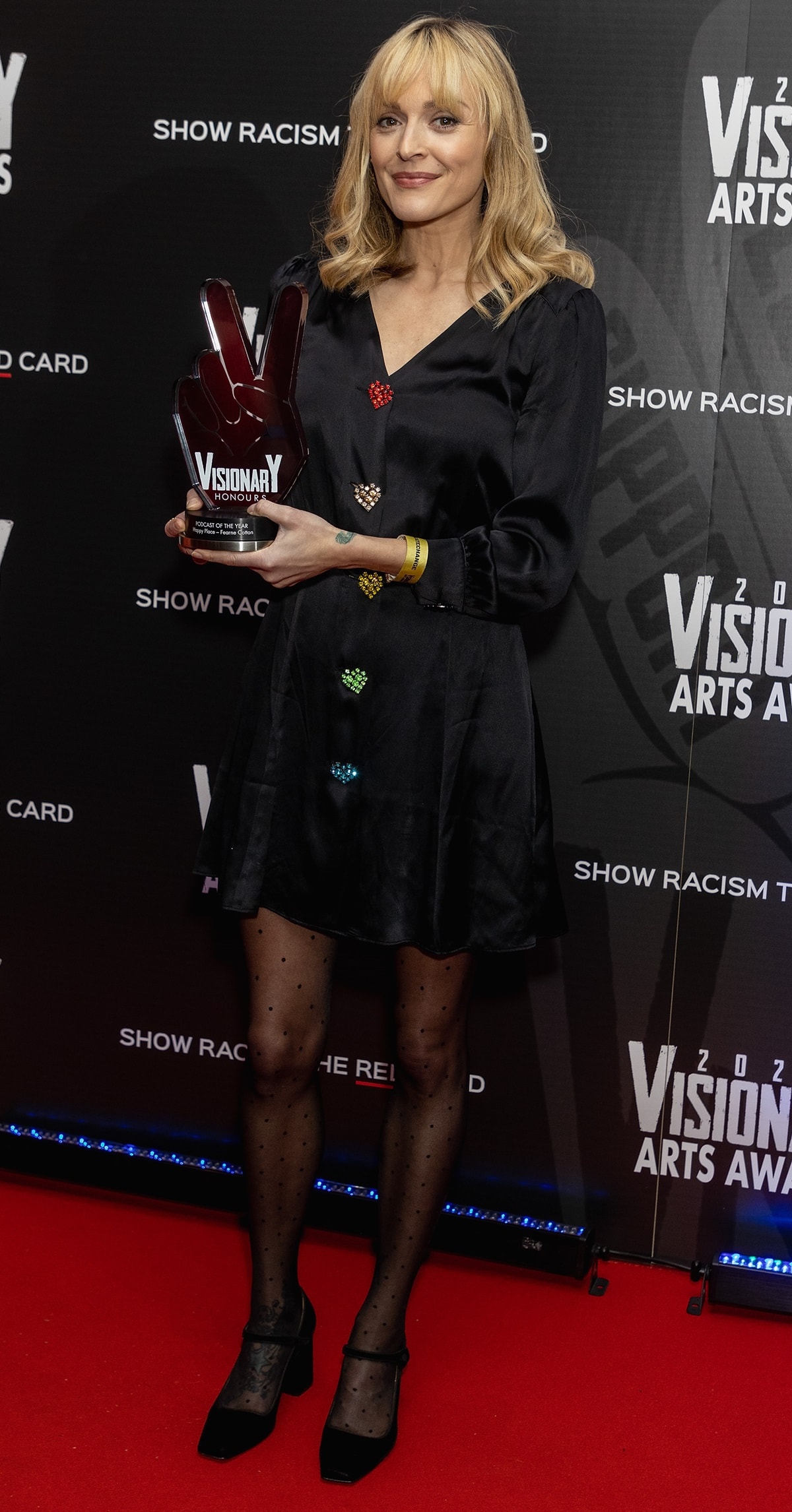 Fearne Cotton stuns in a black satin mini dress with colorful embellishments, polka-dot tights, and classic black Mary Jane heels at the 2023 Visionary Arts Awards