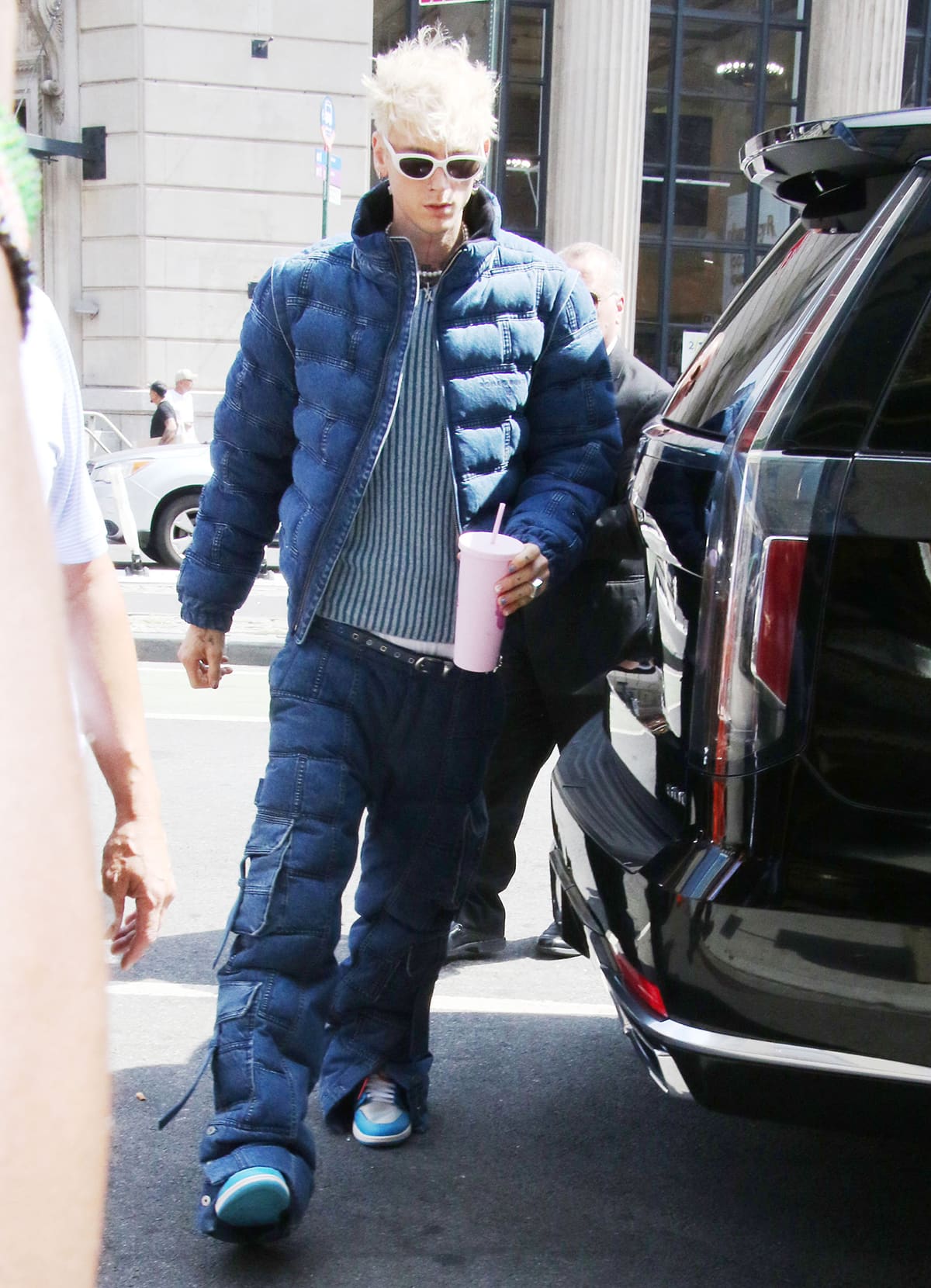 Machine Gun Kelly steps out in a coordinated denim-on-denim look, pairing a quilted puffer jacket and oversized cargo jeans with blue-and-white sneakers that echo the outfit’s cool-toned palette