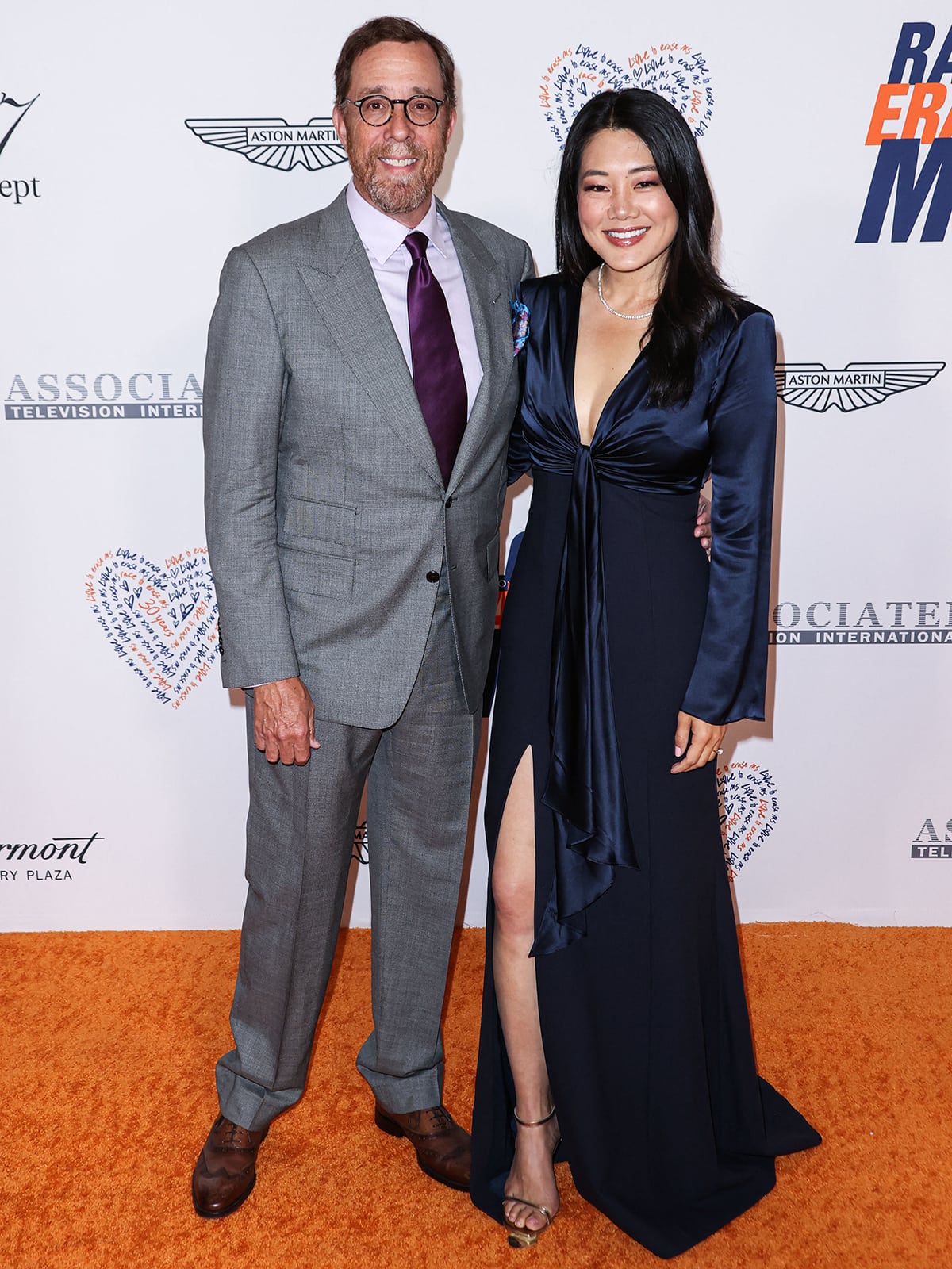 Crystal Kung Minkoff exudes elegance in a deep navy satin gown with a plunging neckline and thigh-high slit, paired with delicate ankle-strap heels, as she poses alongside husband Rob Minkoff at the Race to Erase MS gala