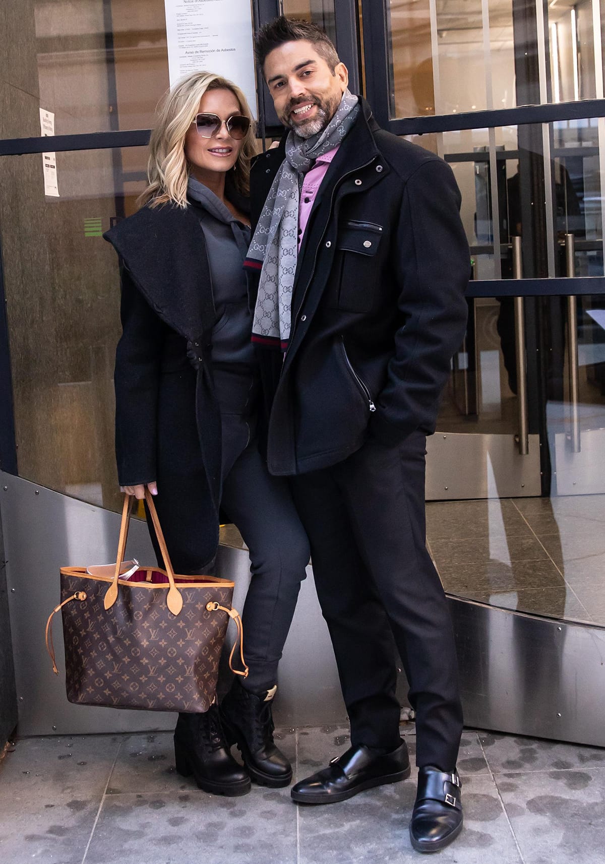 Tamra Judge keeps it chic in a charcoal-toned fitted ensemble with lace-up combat boots and a Louis Vuitton Neverfull tote, stepping out stylishly with husband Eddie Judge
