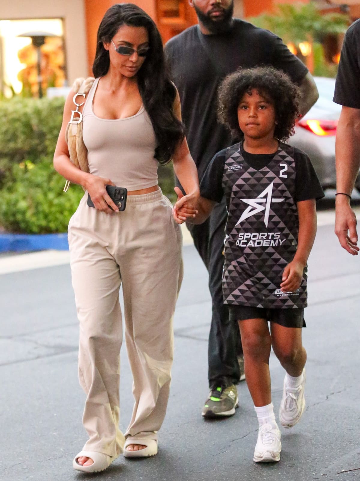 Kim Kardashian wearing Yeezy “Bone” slides and Saint West wearing a basketball jersey, black shorts, white socks, and white Nike sneakers