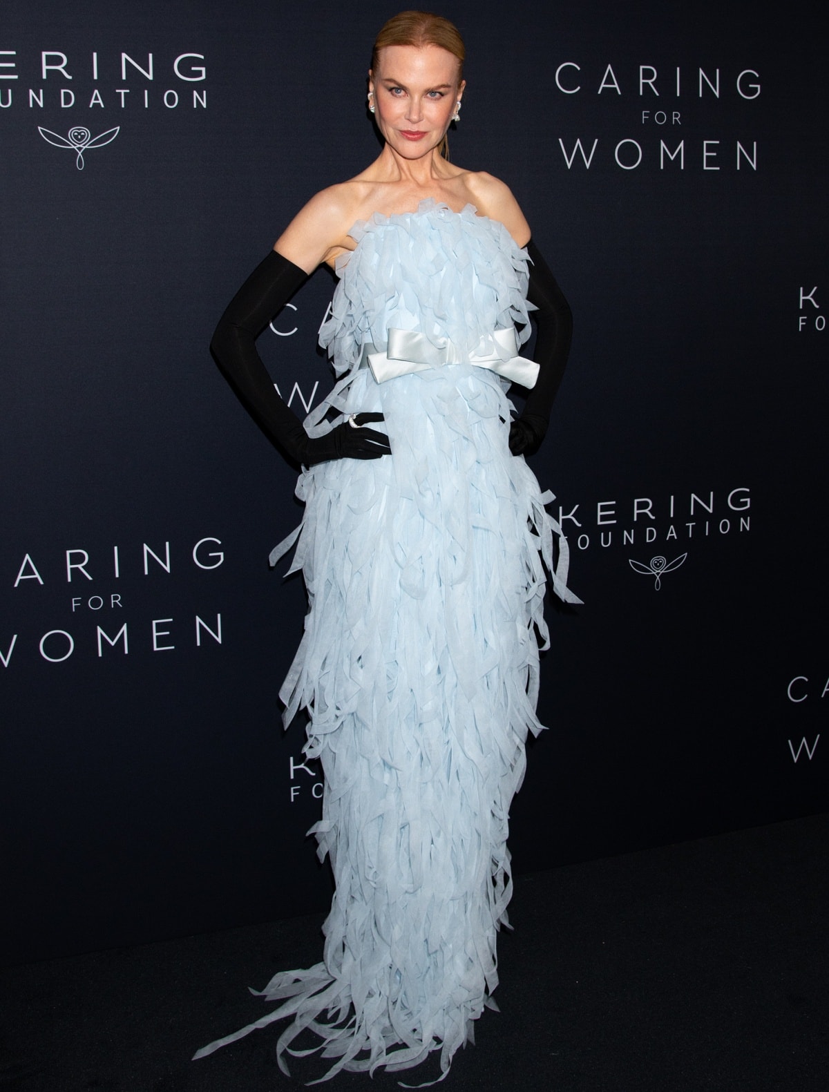 Nicole Kidman exudes timeless elegance in a pale-blue Balenciaga Haute Couture gown adorned with feather-like appliqués, a satin bow accent, and paired with dramatic black opera gloves and diamond jewelry at the Kering Foundation’s Caring for Women Dinner in New York City