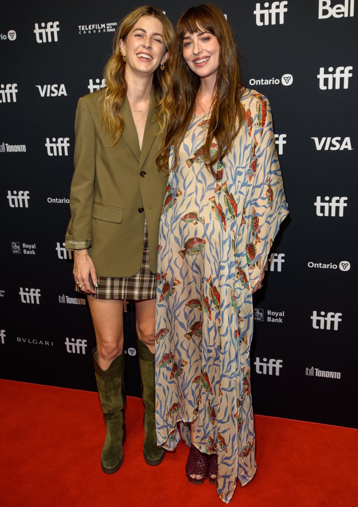 Dakota Johnson pairs her whimsical fish-print Bode kaftan with Bordeaux Bottega Veneta knot mule sandals while Ro Donnelly complements her olive blazer and plaid mini skirt with knee-high suede boots at the Daddio premiere