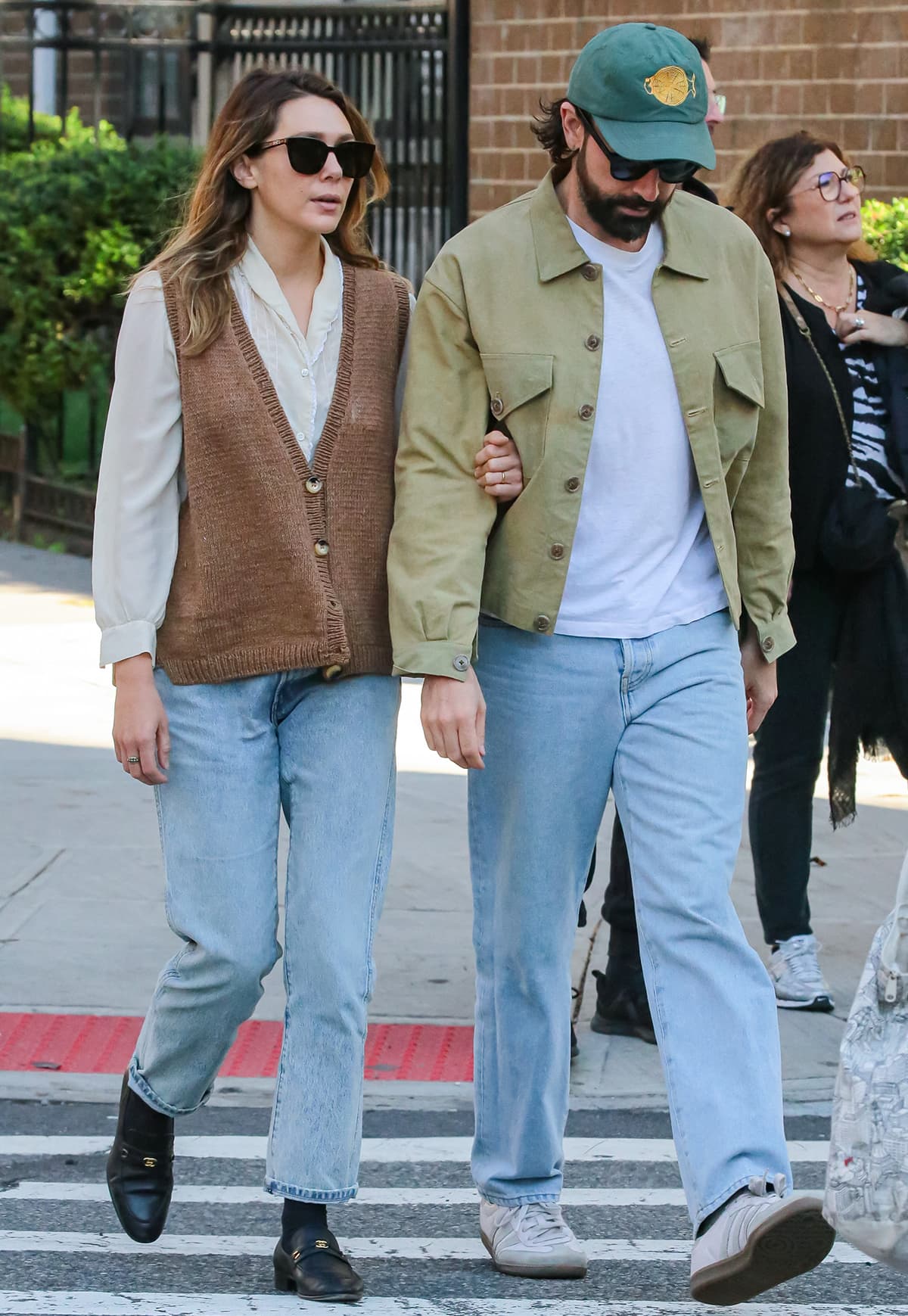 Elizabeth Olsen embraces a casual bohemian vibe in a cream long-sleeved blouse, brown vest, light-washed jeans, and black Chanel loafers