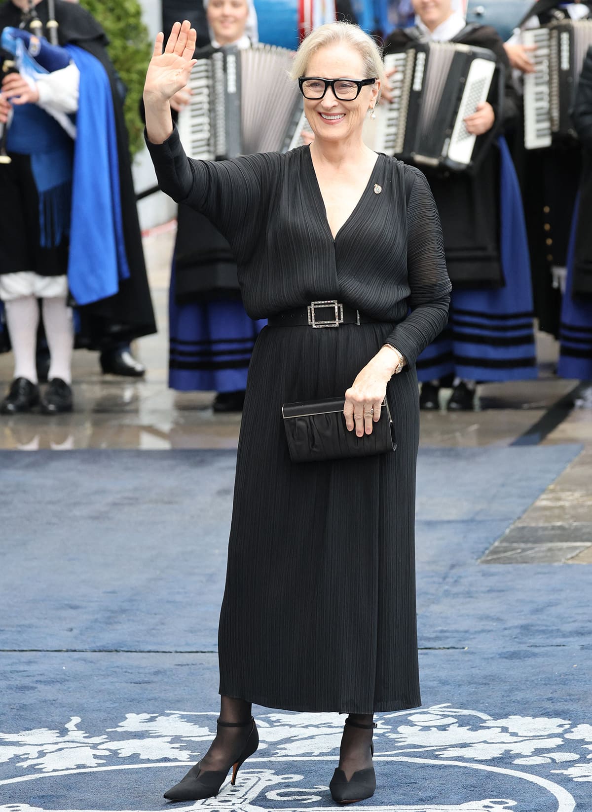 Meryl Streep embraces quiet luxury in a black pleated midi dress cinched with a crystal-buckled belt, pairing it elegantly with sheer tights and pointed ankle-strap heels at the Princess of Asturias Awards