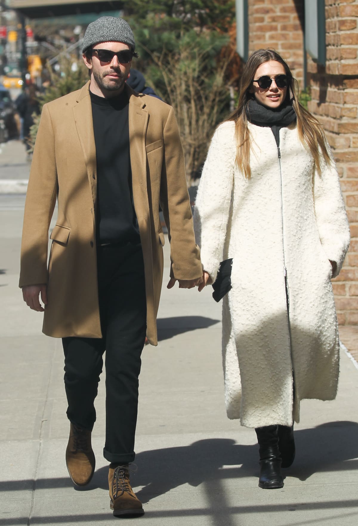 Elizabeth Olsen and Robbie Arnett hold hands while strolling through New York City on March 20, 2017, with Olsen chic in a textured white Sportmax coat and black boots and Arnett coordinating in a camel overcoat and brown lace-up boots