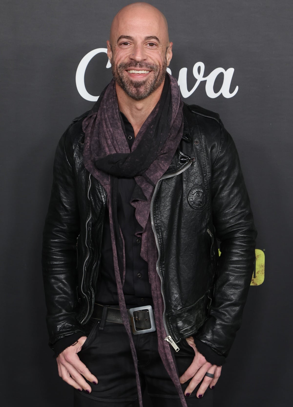 Chris Daughtry rocks an edgy all-black ensemble featuring a textured leather jacket, layered scarf, and dark denim at a red carpet event, blending rugged style with subtle flair